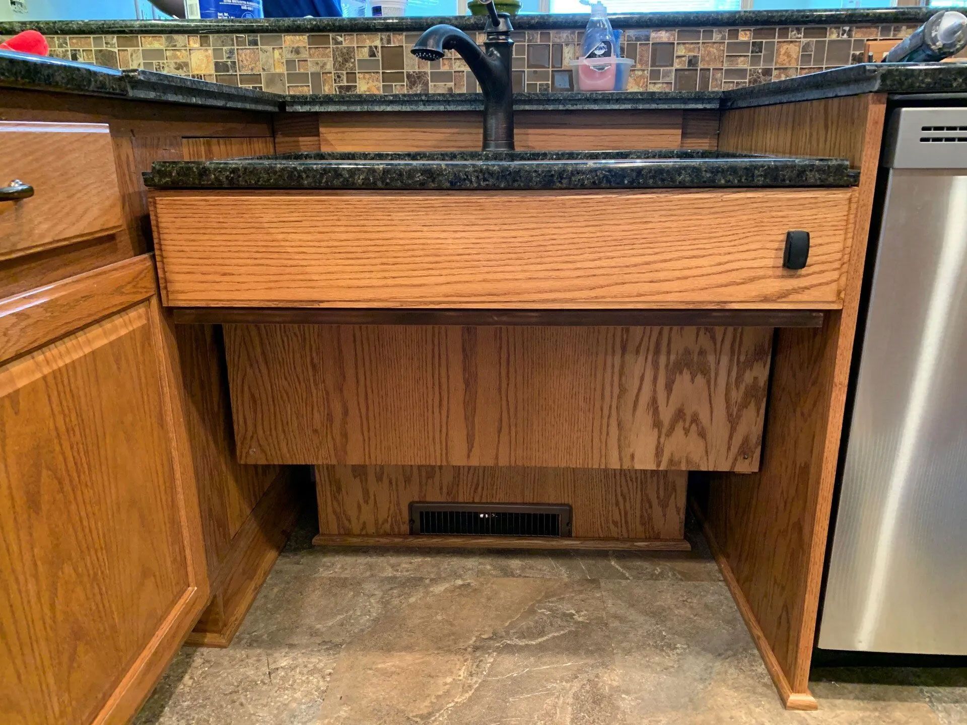 Accessible kitchen sink with open cabinet for wheelchair use. Oak cabinets and dark countertop.