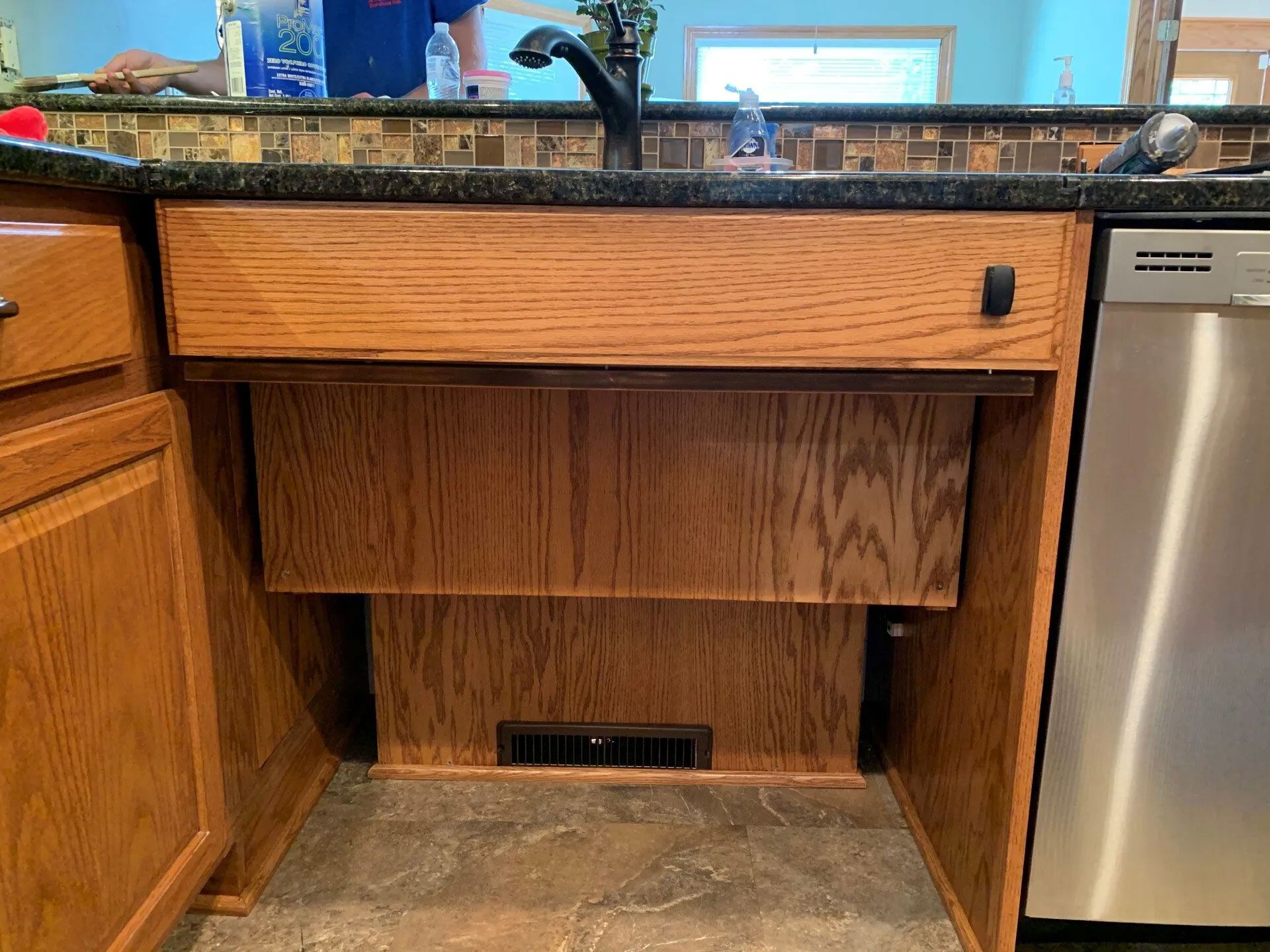 Kitchen sink base with a drawer, cabinet doors, and a dishwasher to the right. Wood cabinets.