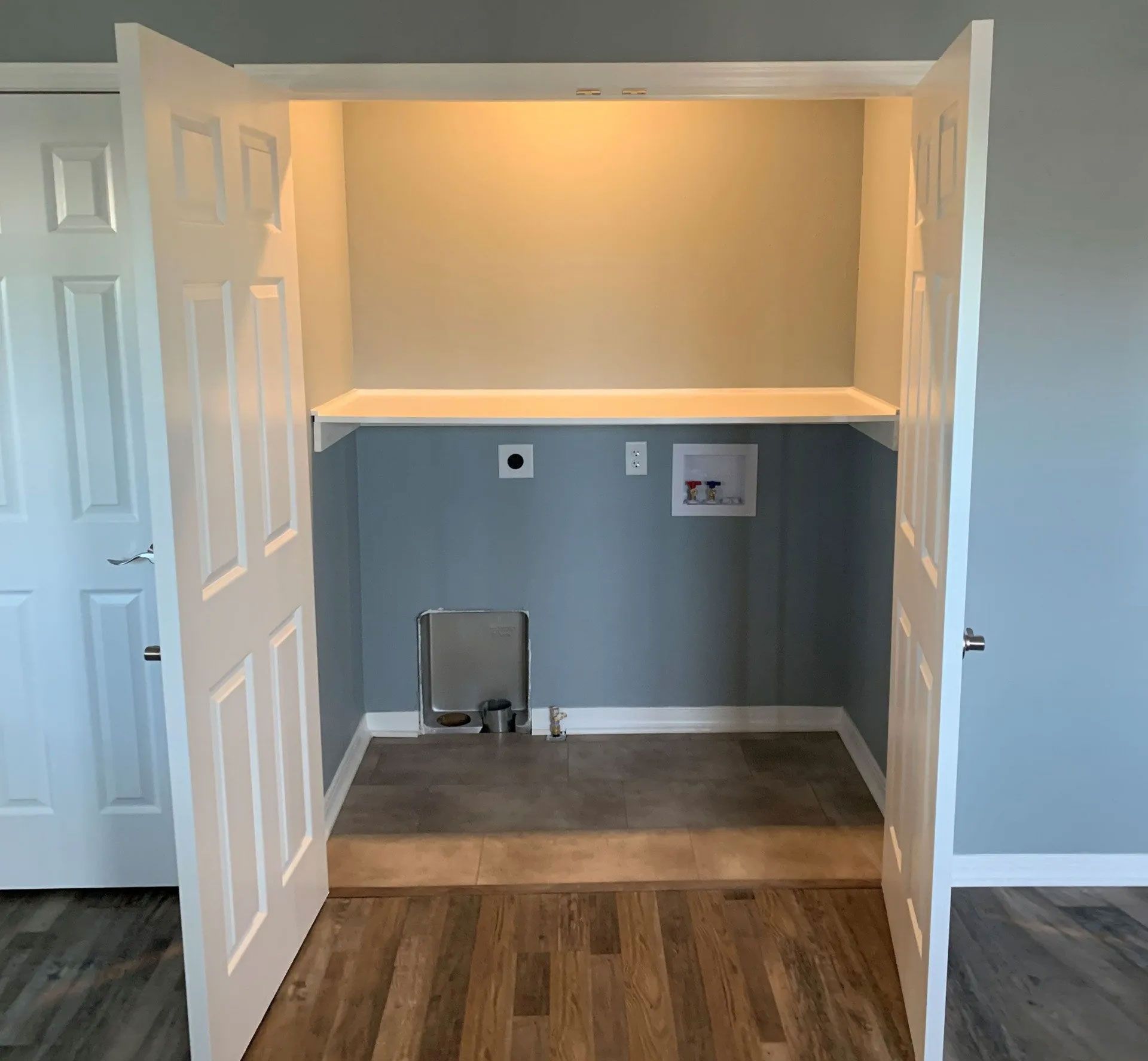 Laundry closet with doors open, featuring shelf, water hookups, and electrical outlet.