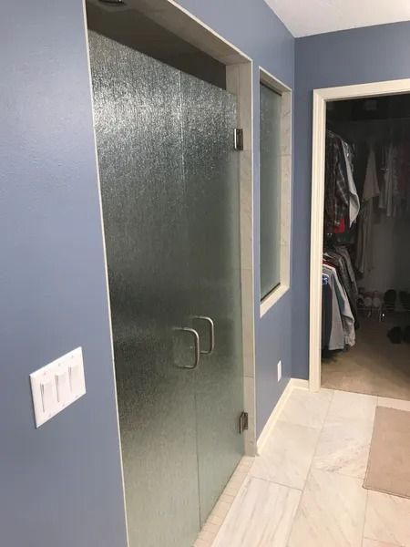 Blue-walled bathroom with frosted glass shower door, a small window, and a door leading to a closet.