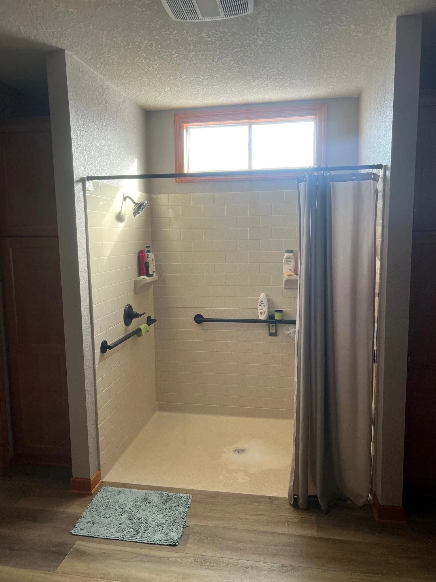 Accessible shower with grab bars and curtain, light tiles, and a small rug on the floor.