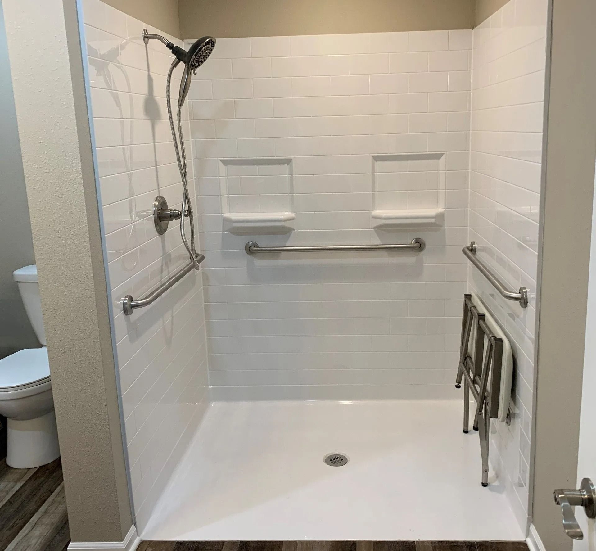Accessible white tile shower with grab bars, shower seat, and two built-in shelves.