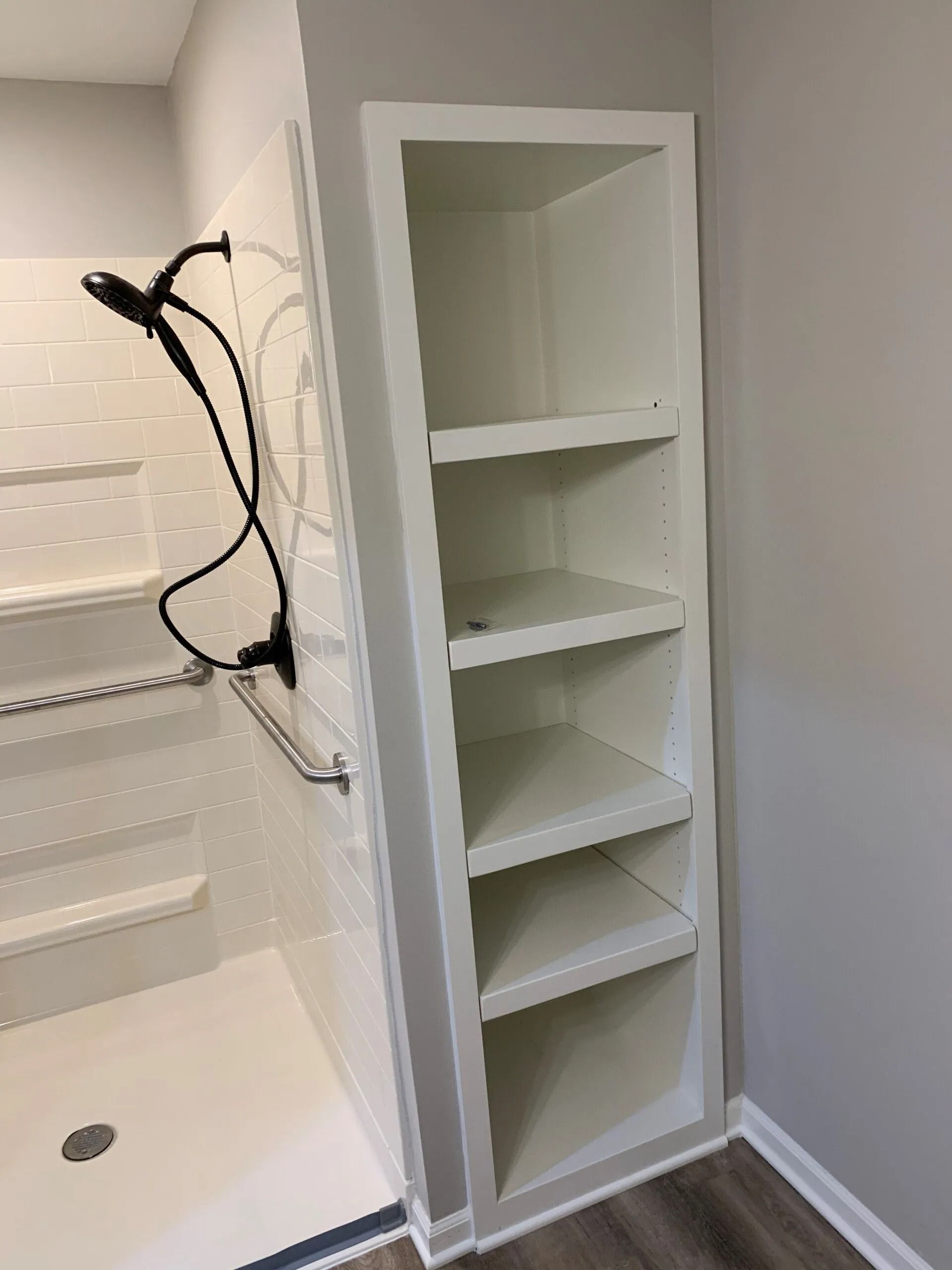 White built-in shelving unit next to a white shower stall with a black shower head and handle.