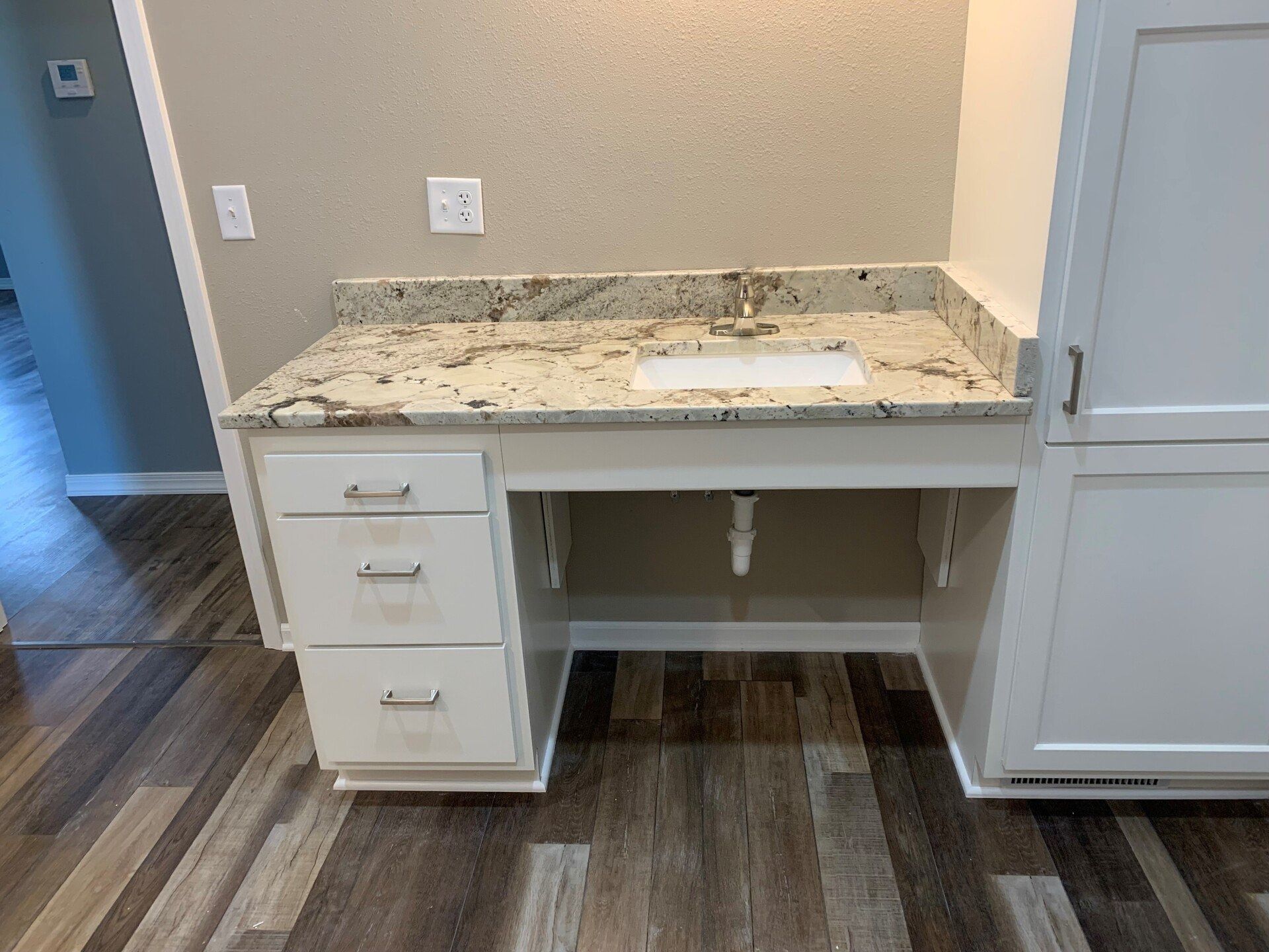 White vanity with granite countertop and accessible knee space, next to storage cabinet.