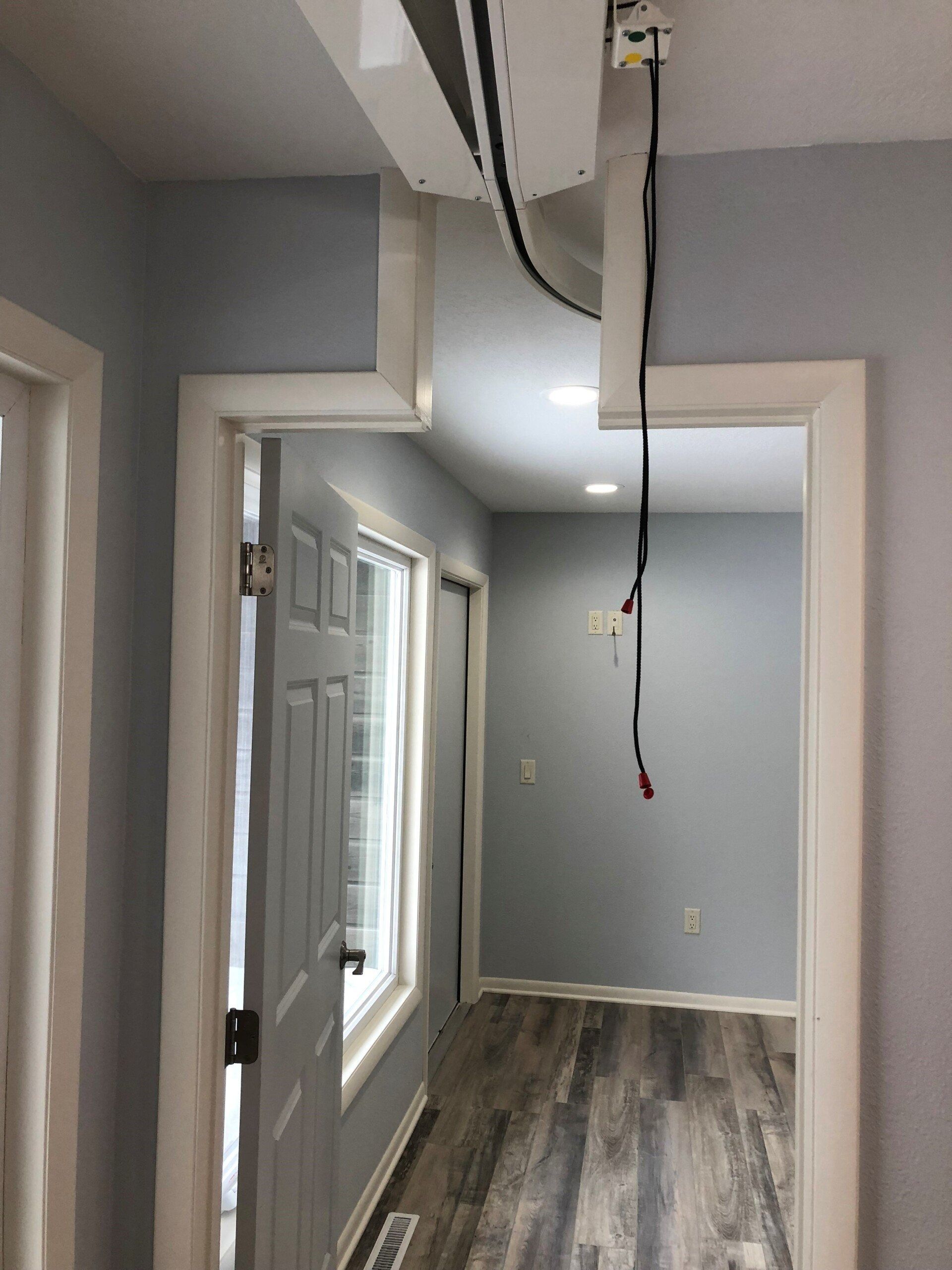 Hallway with a track ceiling lift, gray walls, white trim, and a window.