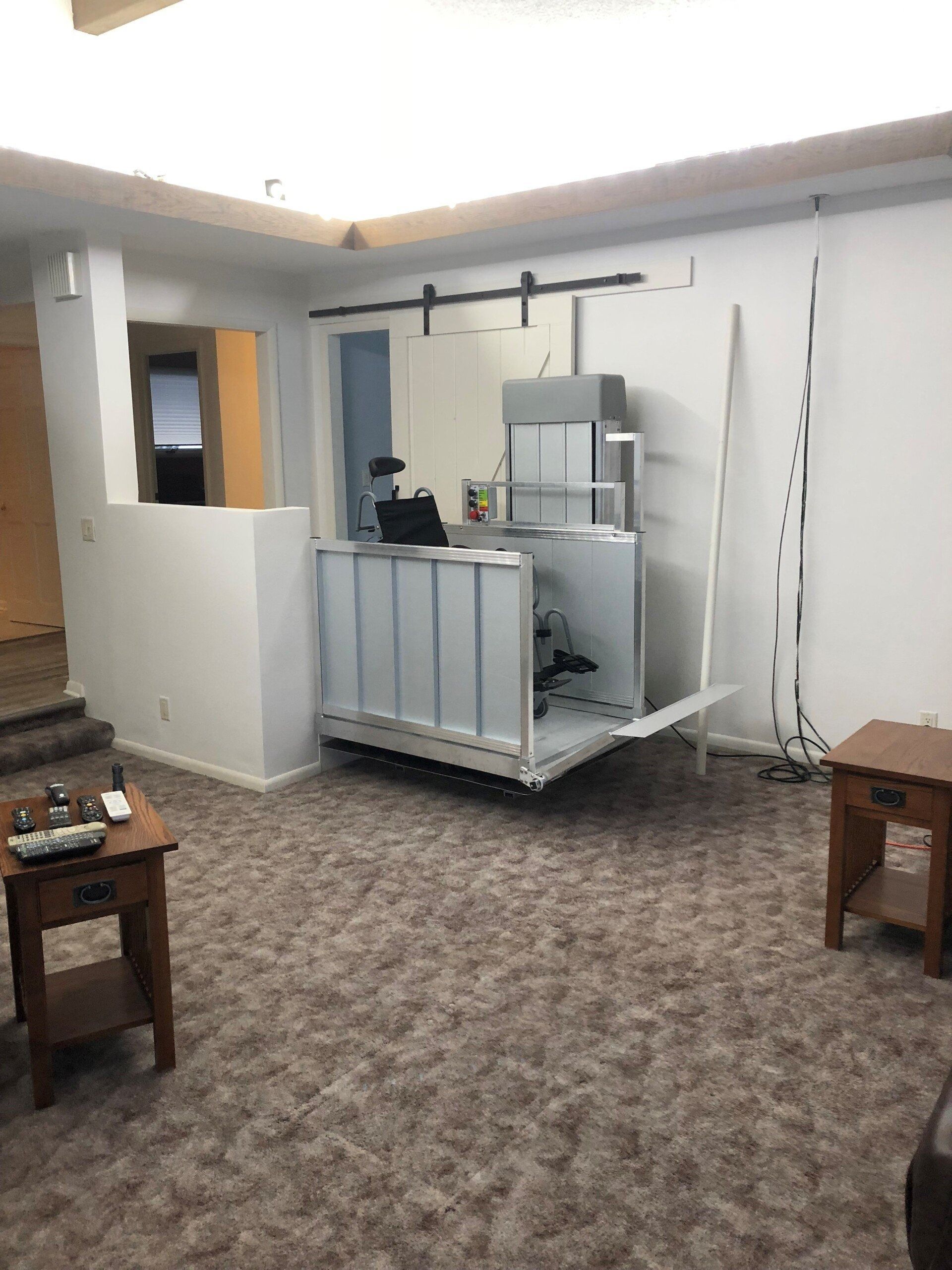A room with a large, white, accessible lift extending out. Carpeted floors, two small end tables.