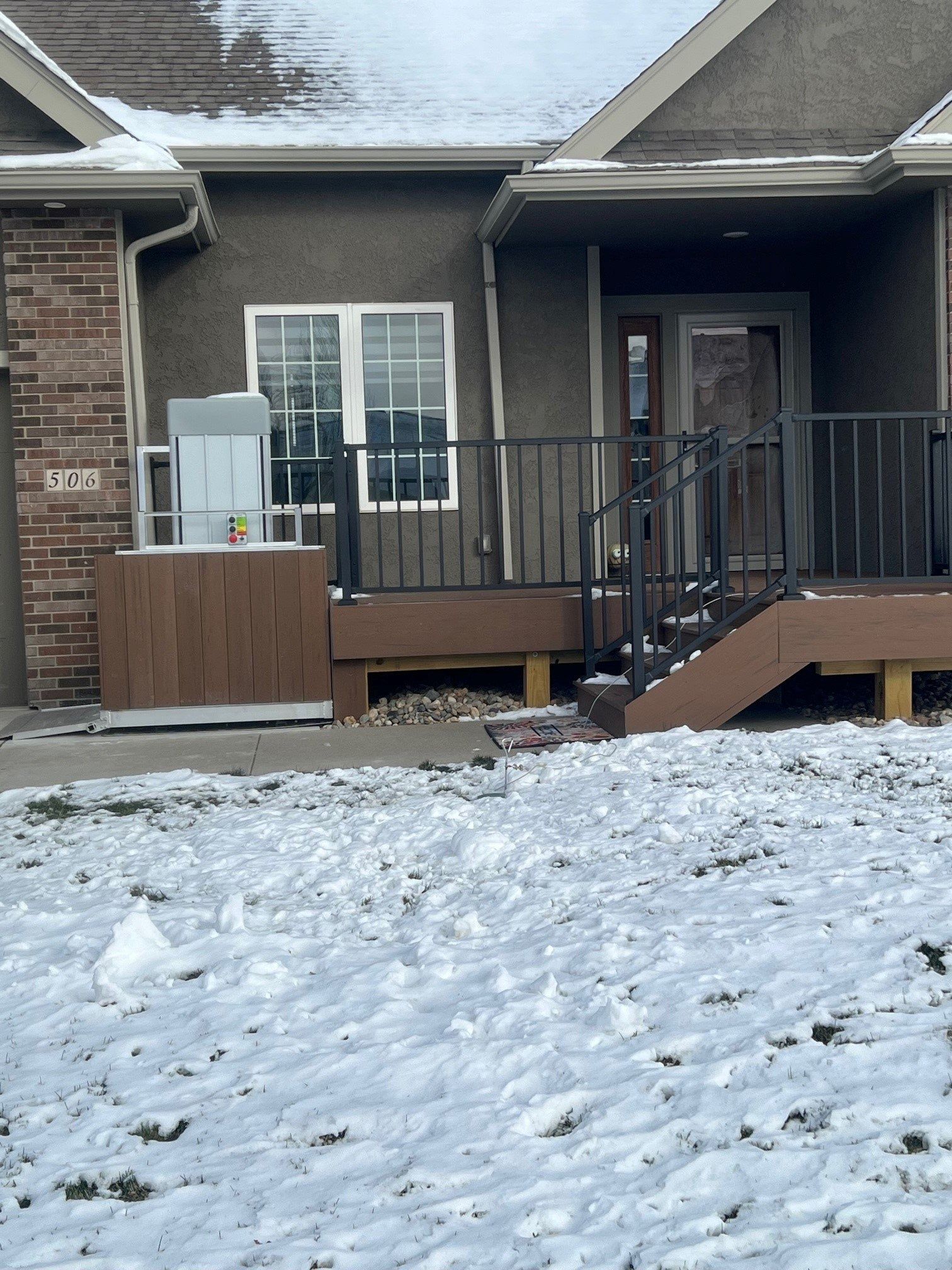 Exterior view of a house with a deck covered in snow. A stair lift is on the deck.