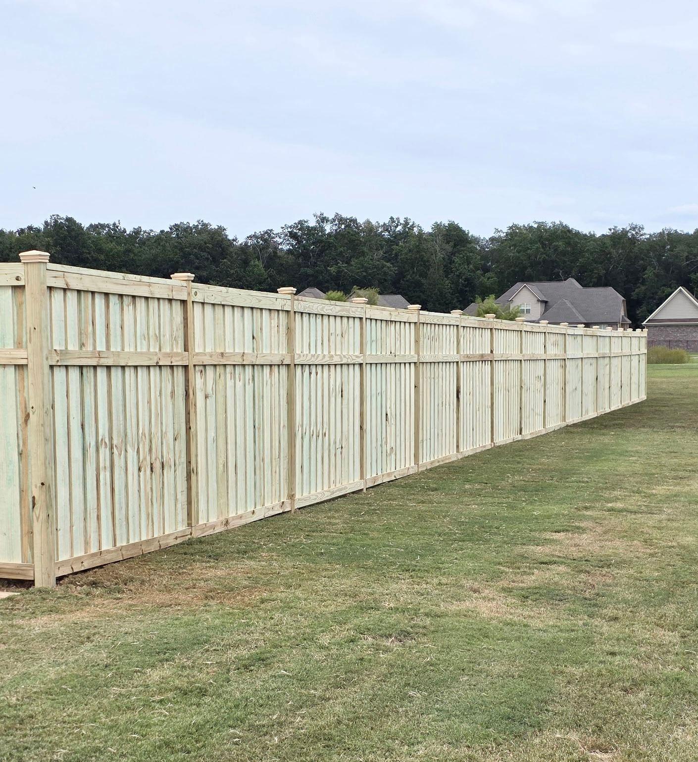 Wooden privacy fence in a grassy yard, under a cloudy sky.