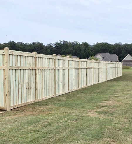 Wooden privacy fence in a grassy yard, under a cloudy sky.