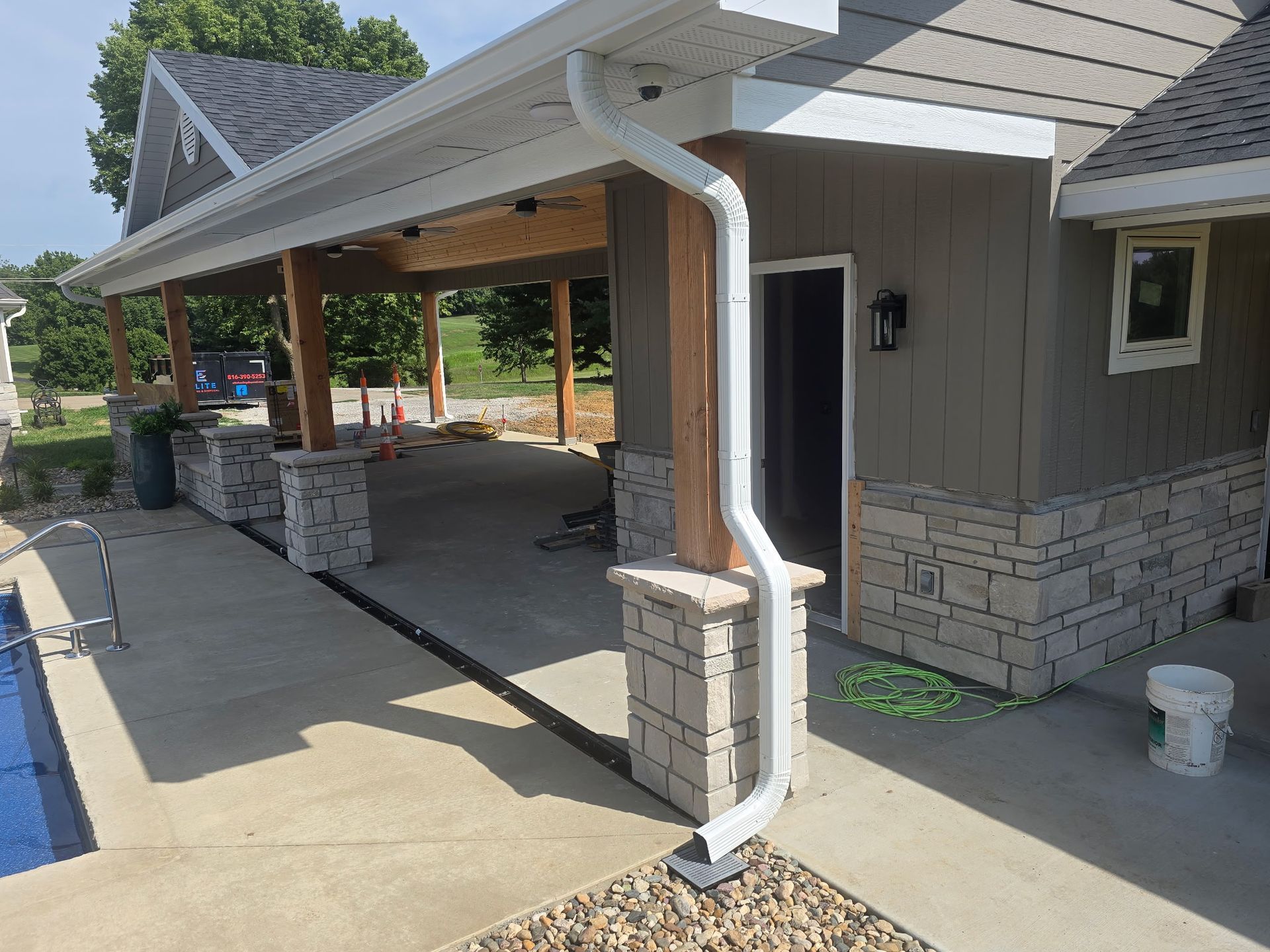 Covered driveway and front porch with white gutters, stone columns, and gray siding at a house