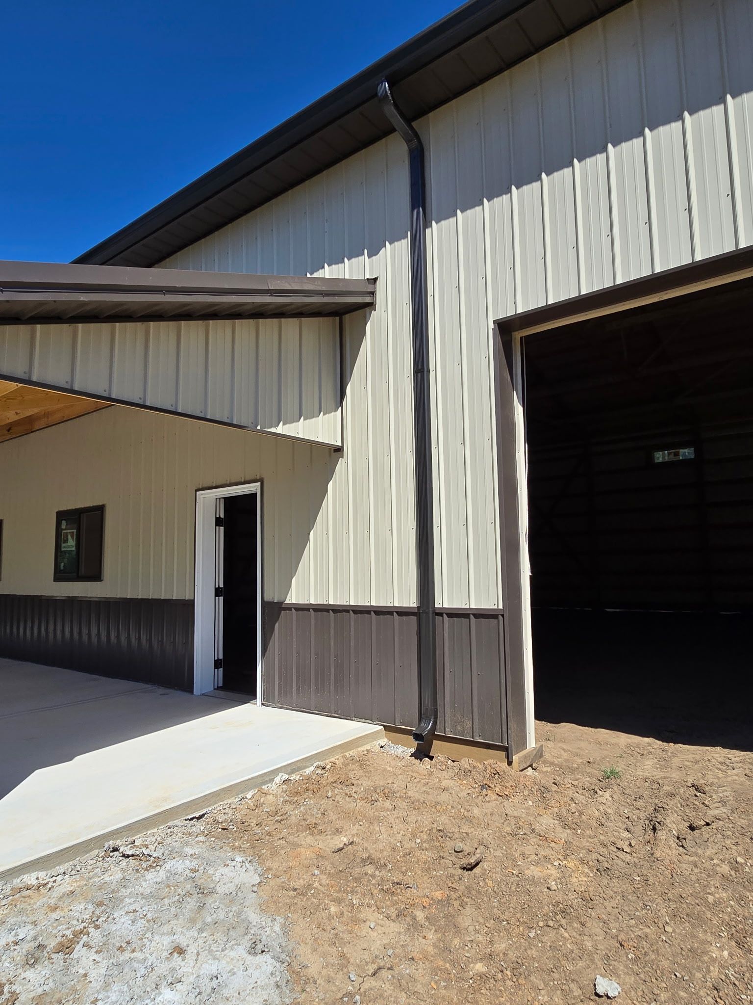 Exterior of a metal building with a covered concrete entryway and open garage door under a blue sky