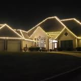 House at night with roof outlined in warm white Christmas lights.