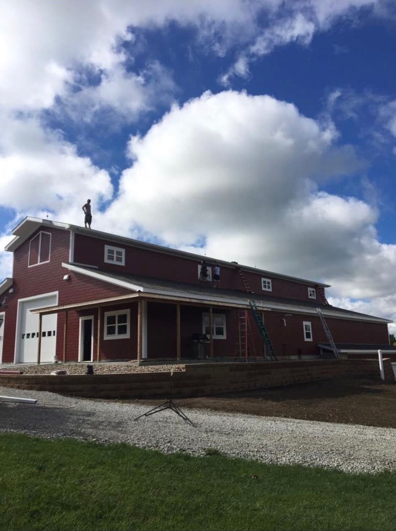 Red barn under construction with a person on the roof against a partly cloudy, blue sky.