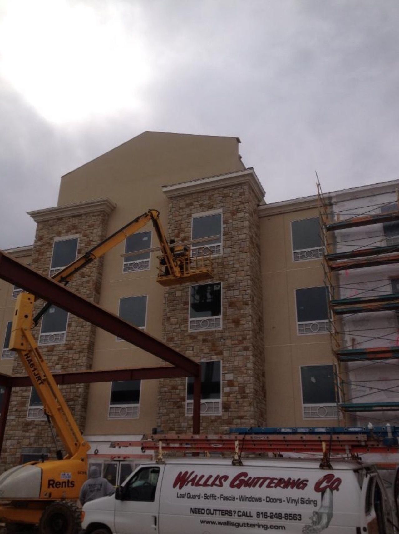 Construction site with a building featuring stone facade and a yellow lift.