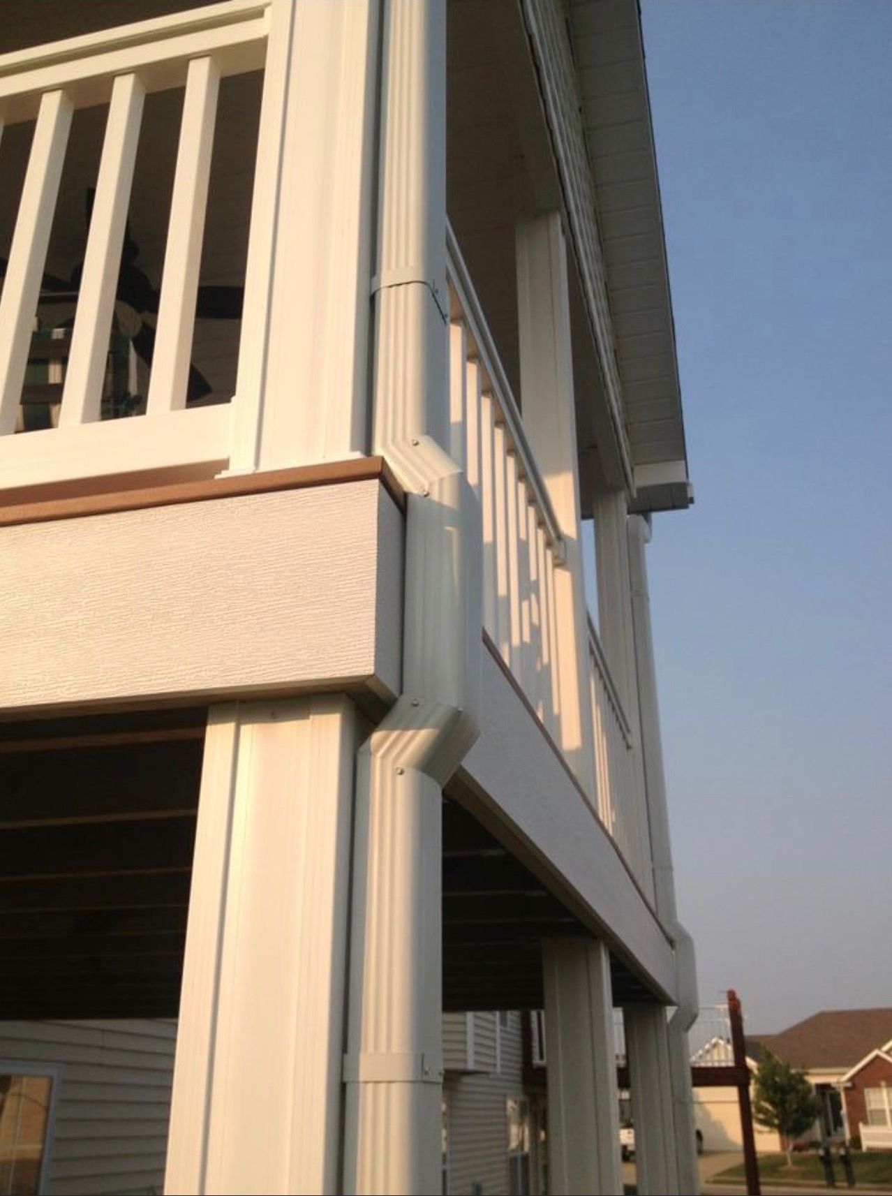 White two-story building with a railing and a gutter system; clear sky in the background.