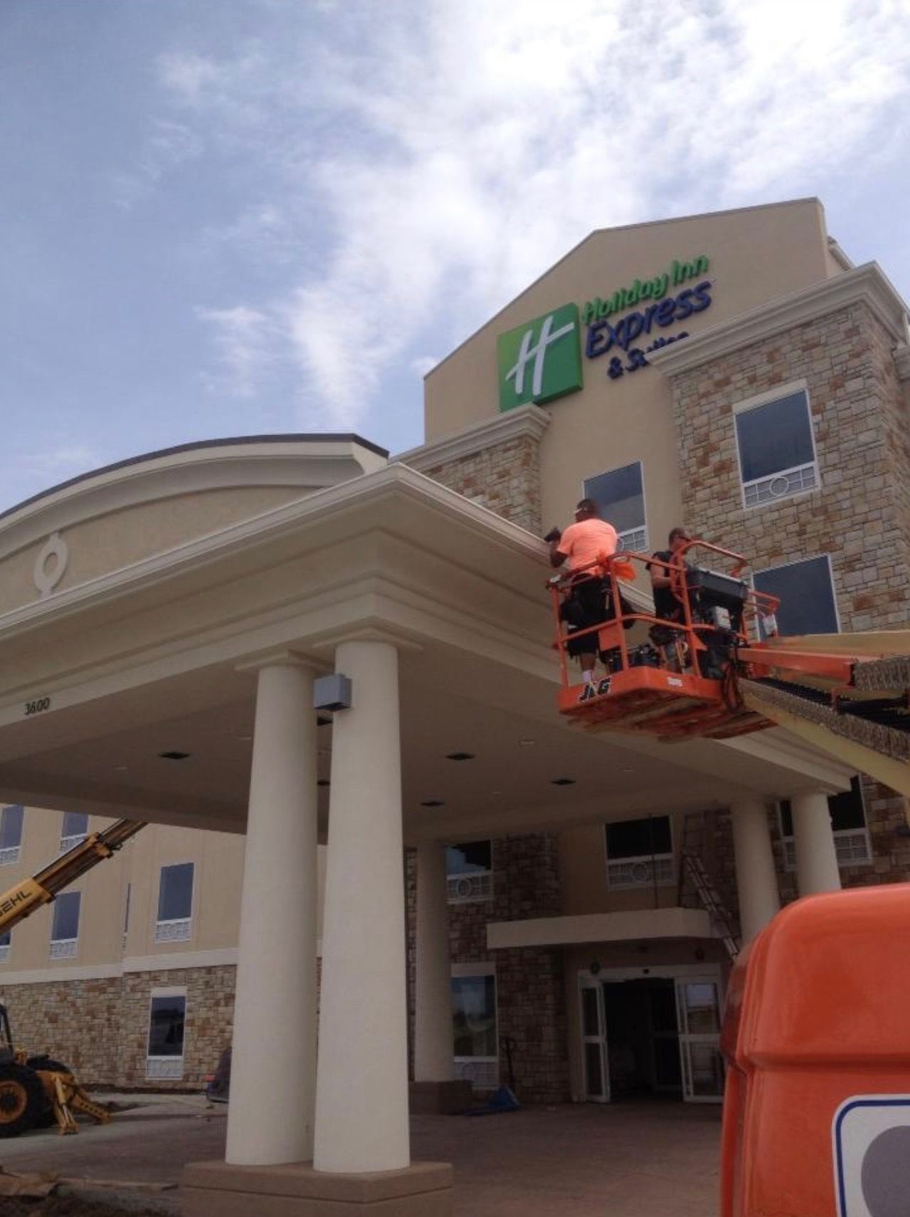 Workers in a lift installing signage on a Holiday Inn Express exterior.