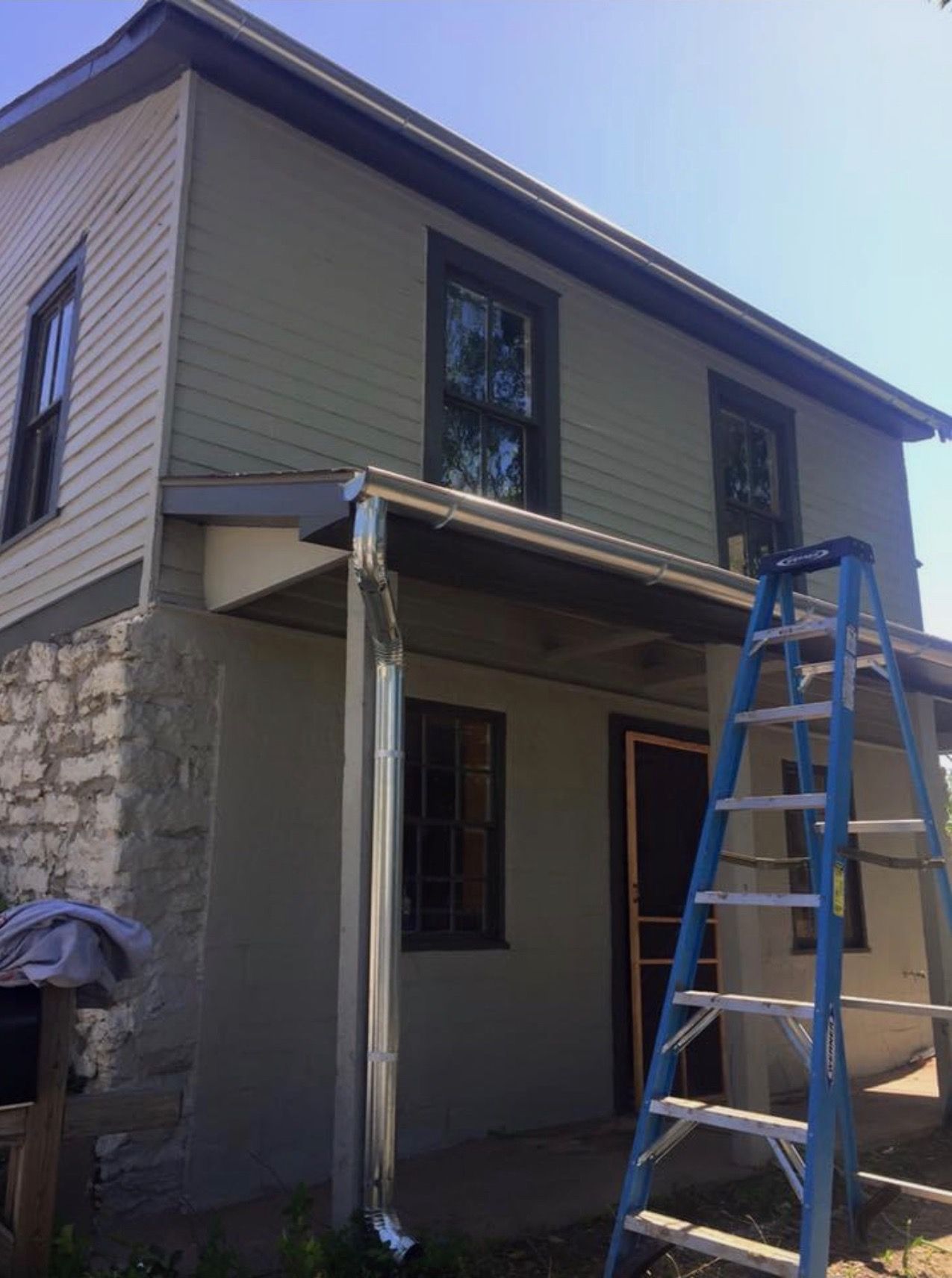 Two-story house with green siding, a small porch, and a blue ladder propped against the side.
