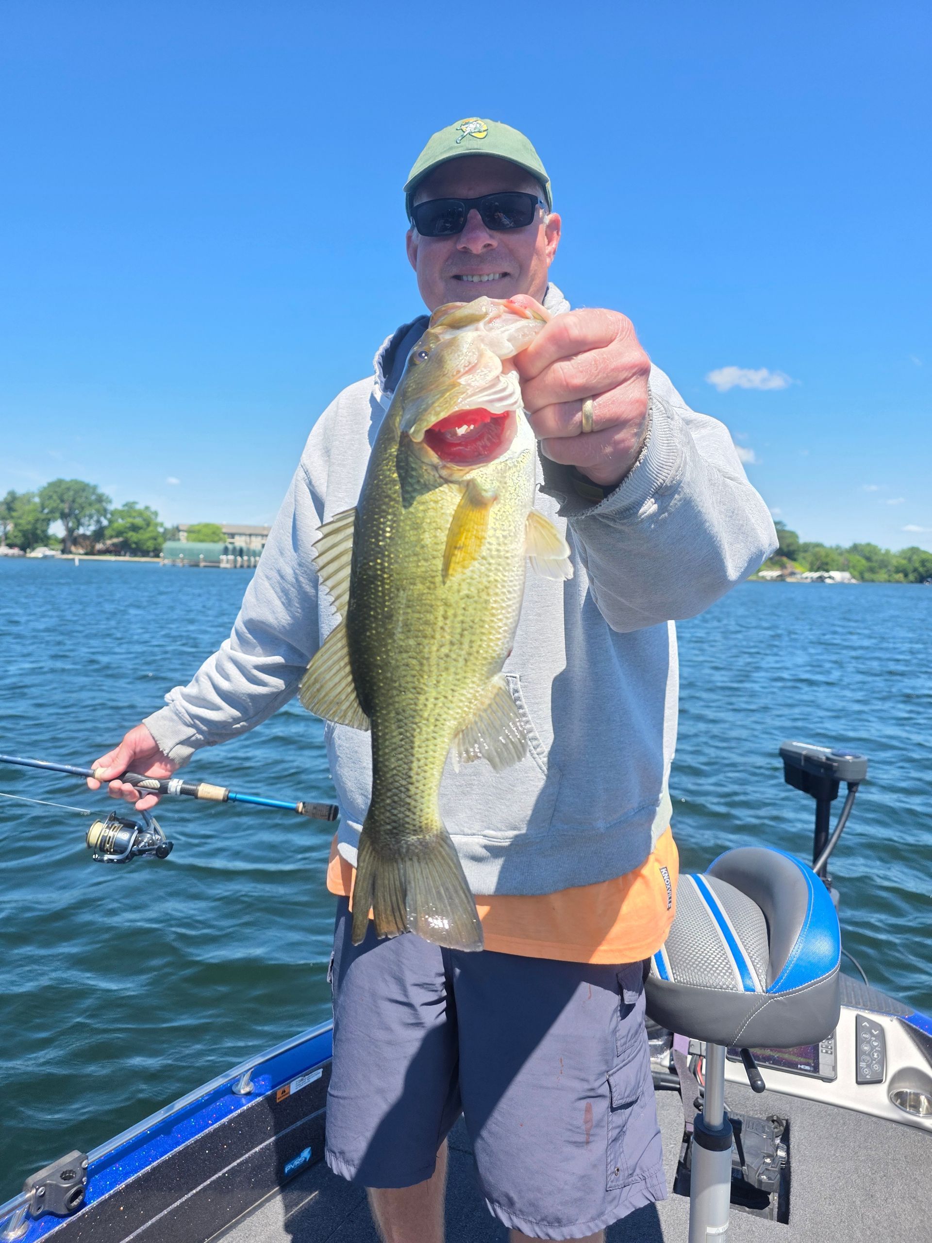 Angler holding a large bass on a boat on a sunny lake, blue sky in the background