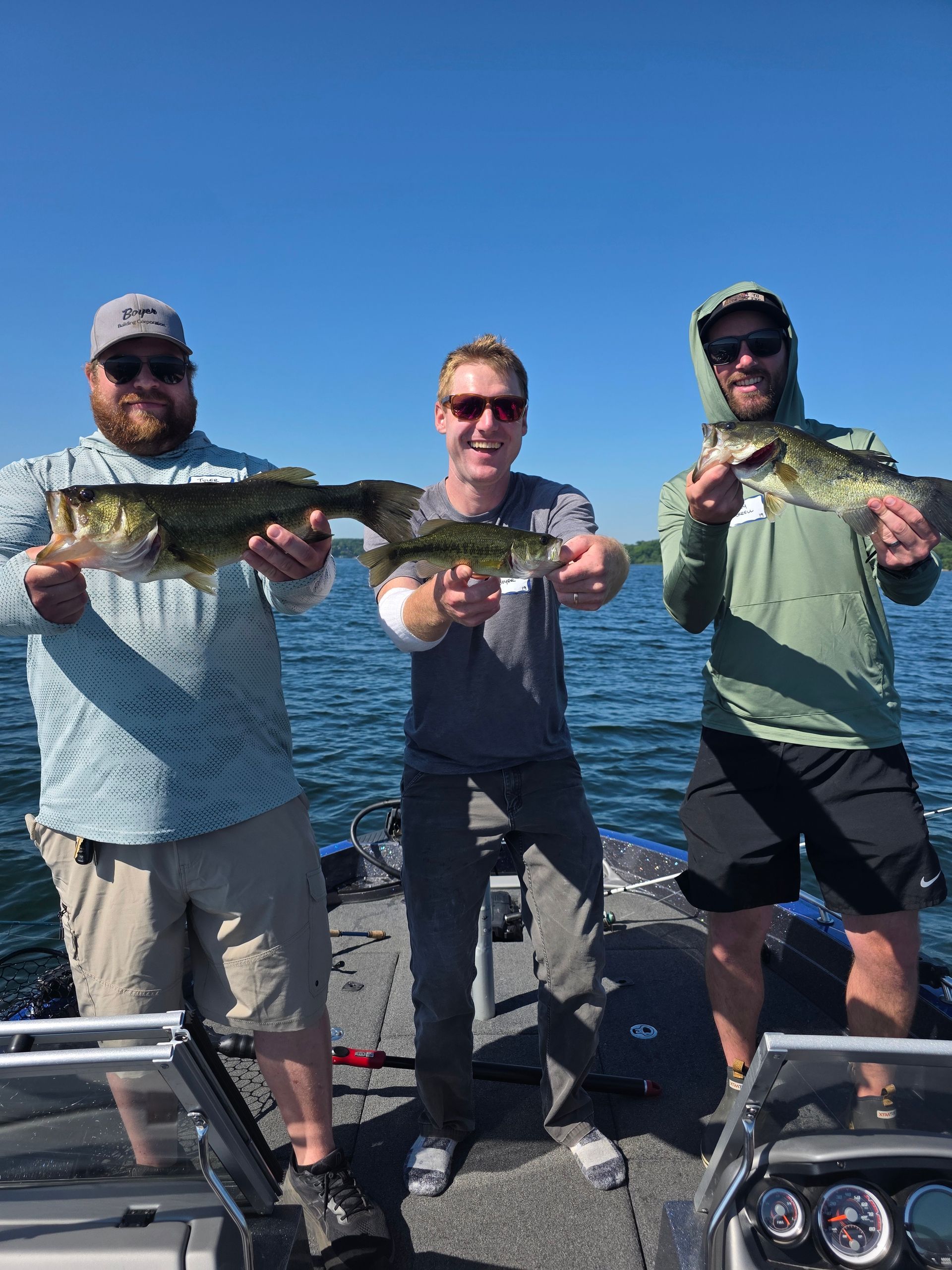 Three anglers on a boat hold up fish on a sunny day with blue water in the background