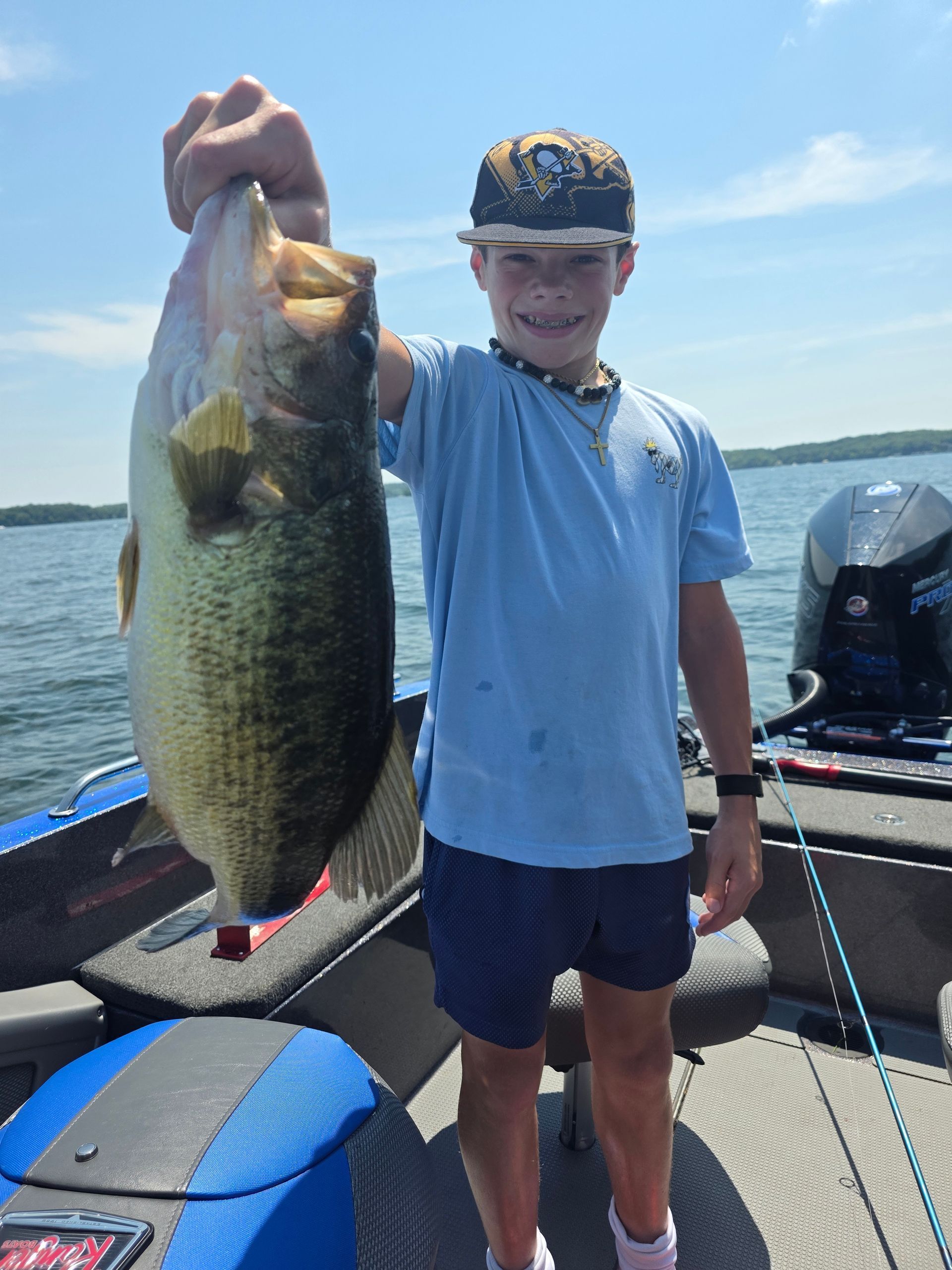 Person on a boat holds up a large fish on a sunny lake.