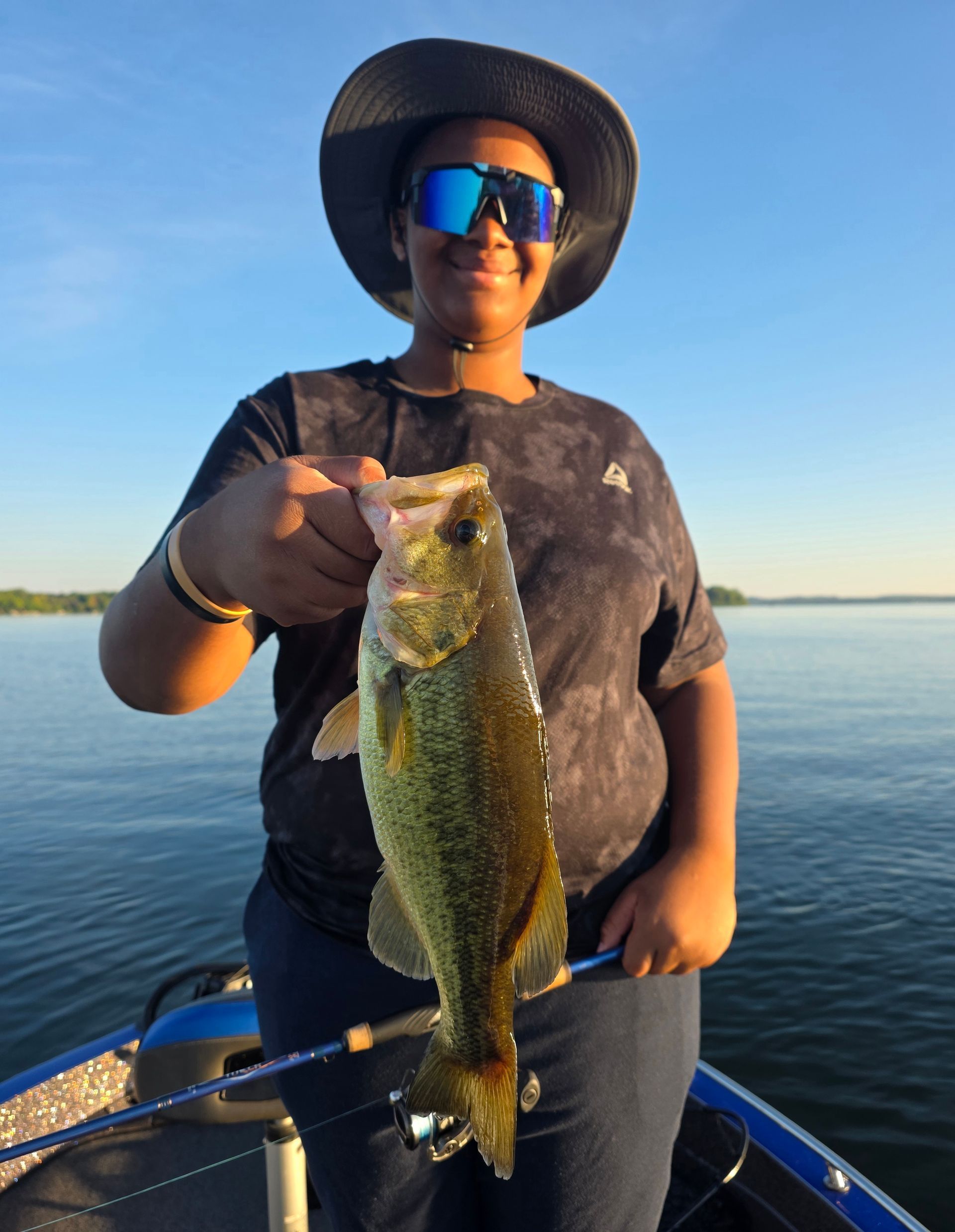Person on a boat holding up a largemouth bass on a calm lake at sunset