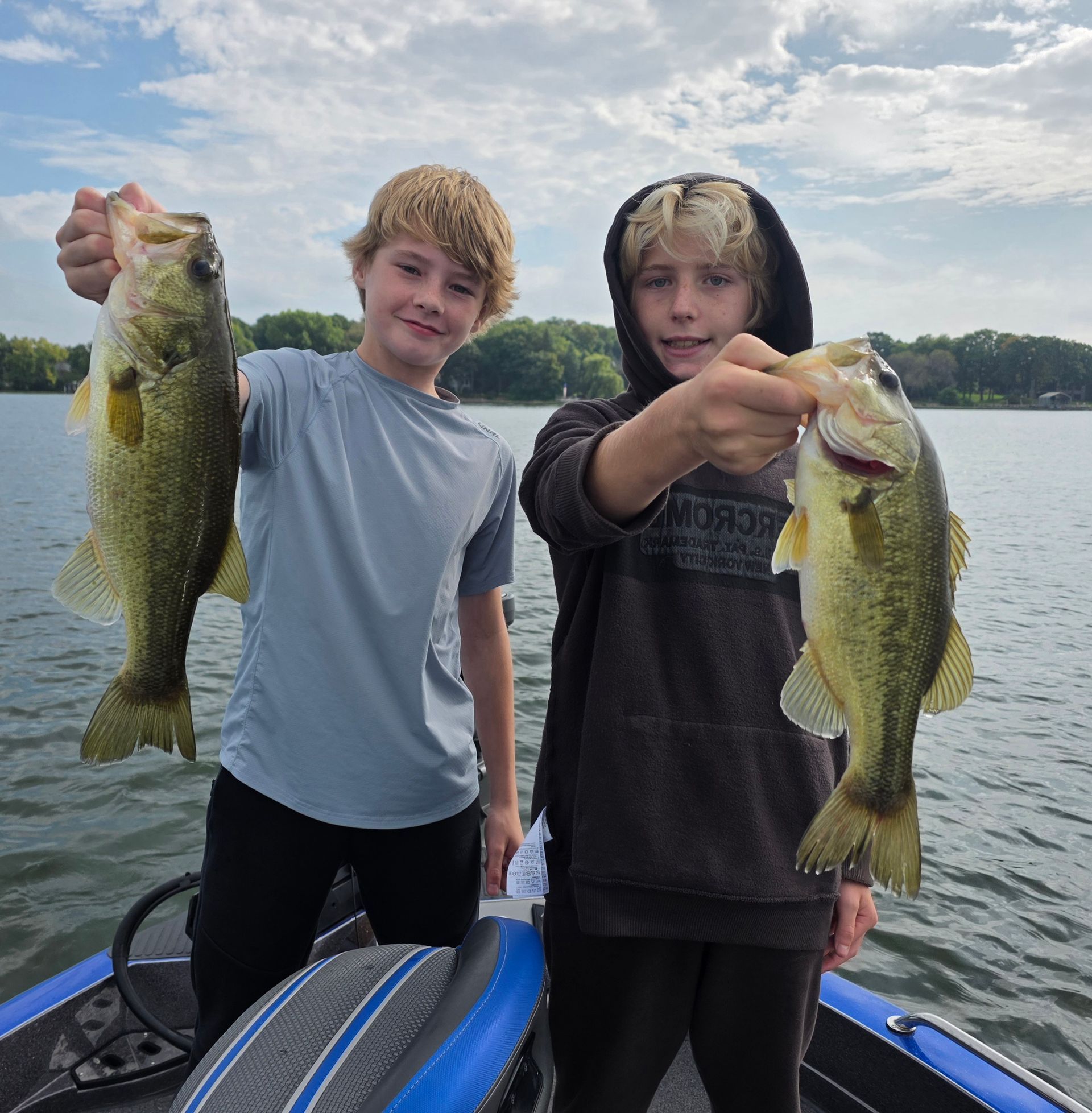 Two people on a boat hold up largemouth bass on a lake under a cloudy sky.