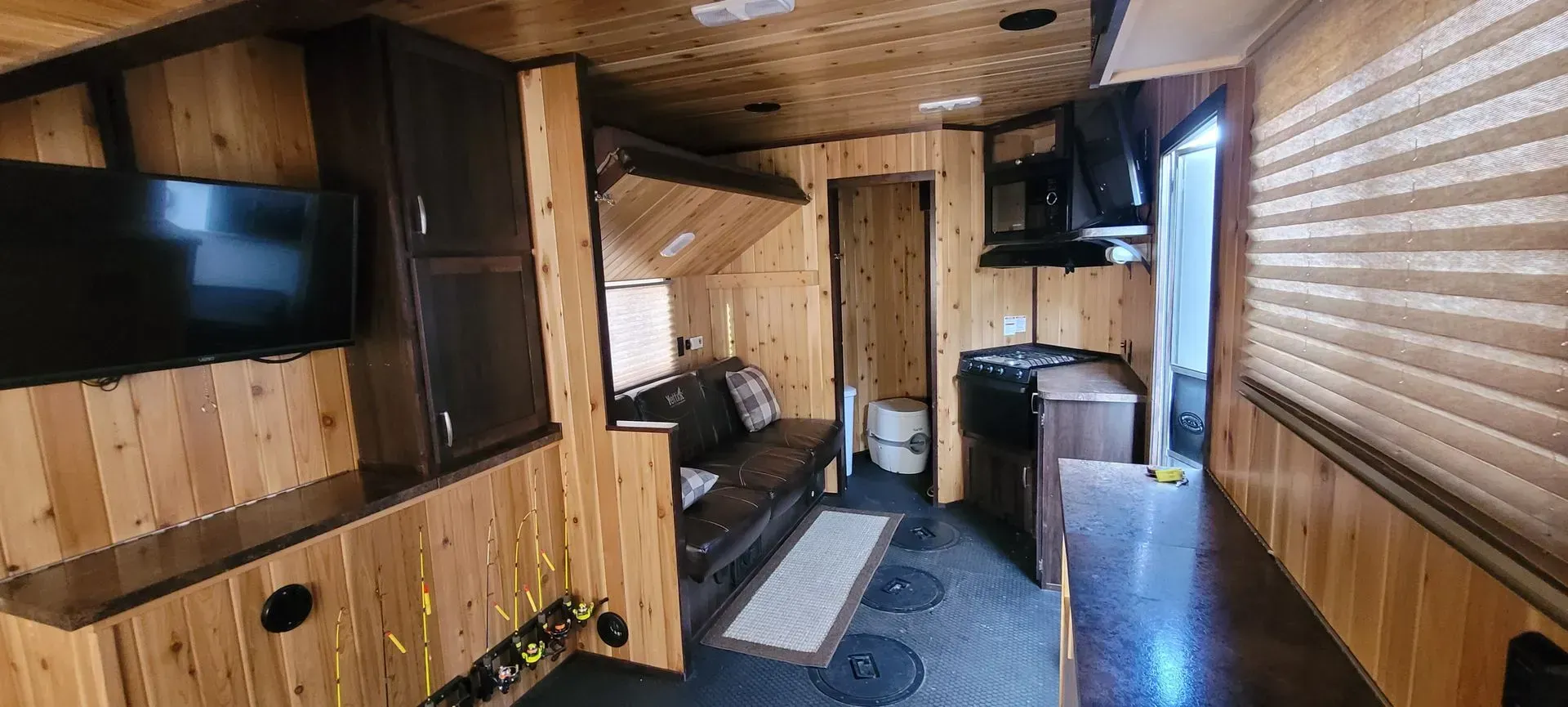 Wood-paneled cabin interior with TV, bunk bed, and bed near a hallway.