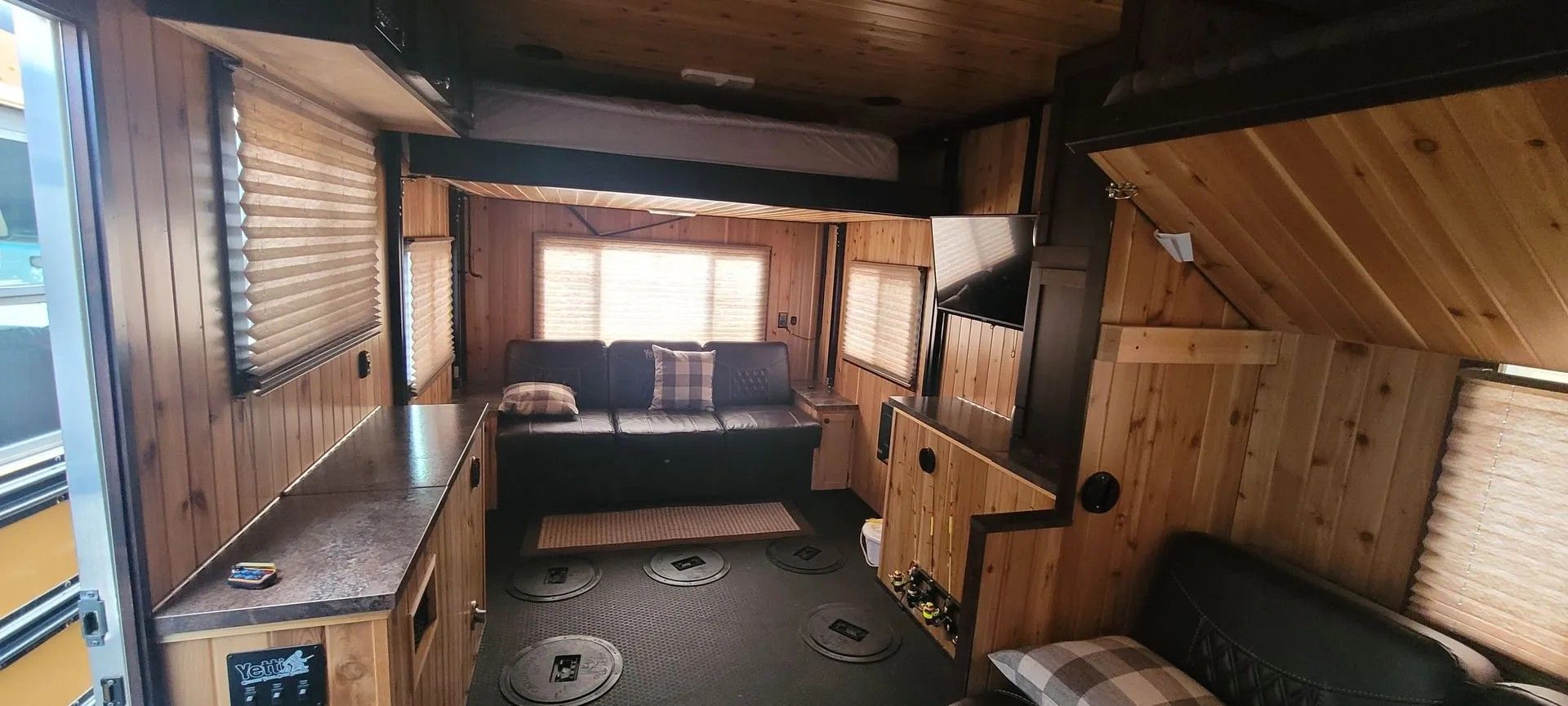 Wood-paneled camper interior with a window bench, table, and compact seating area