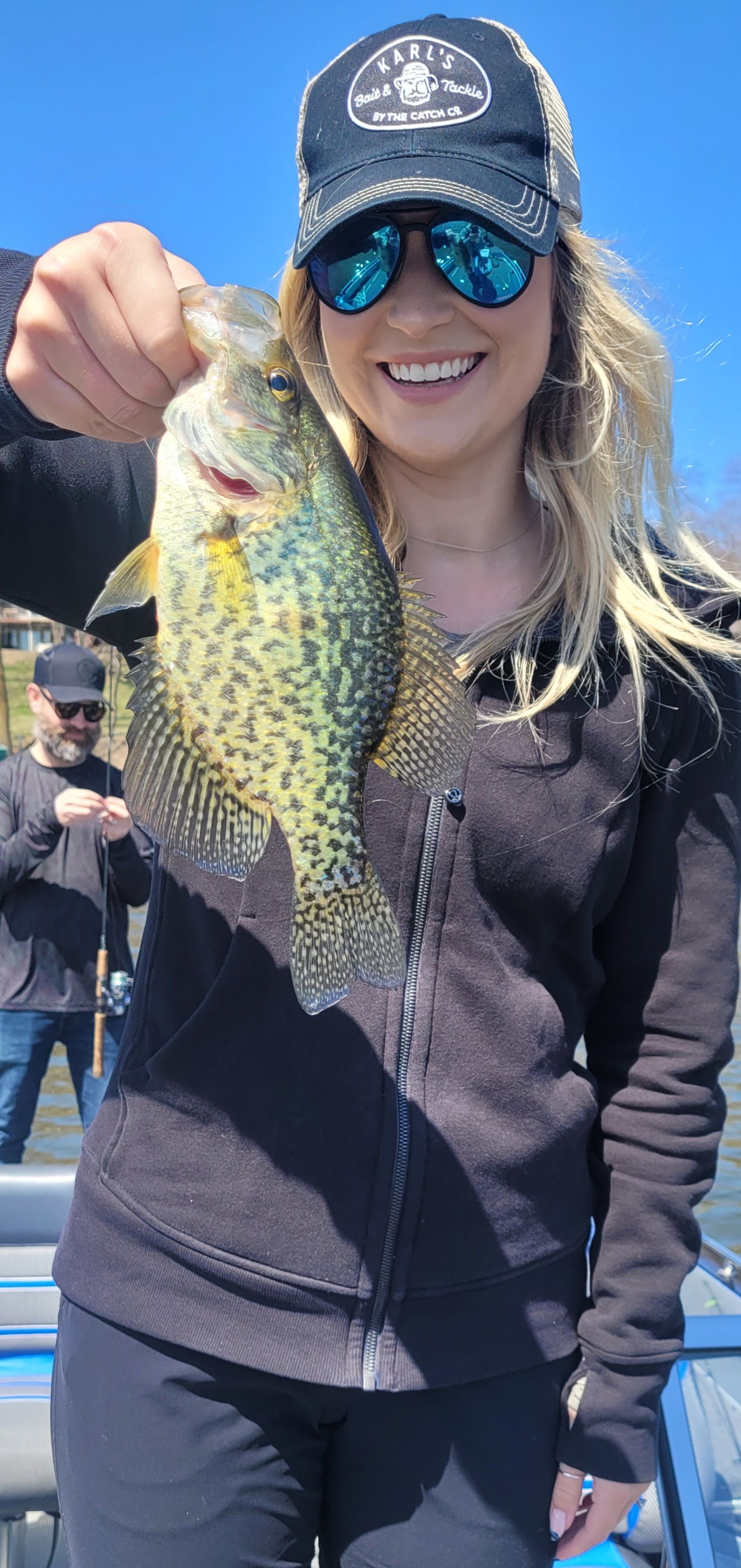 Smiling woman in sunglasses holding a large fish outdoors on a sunny day