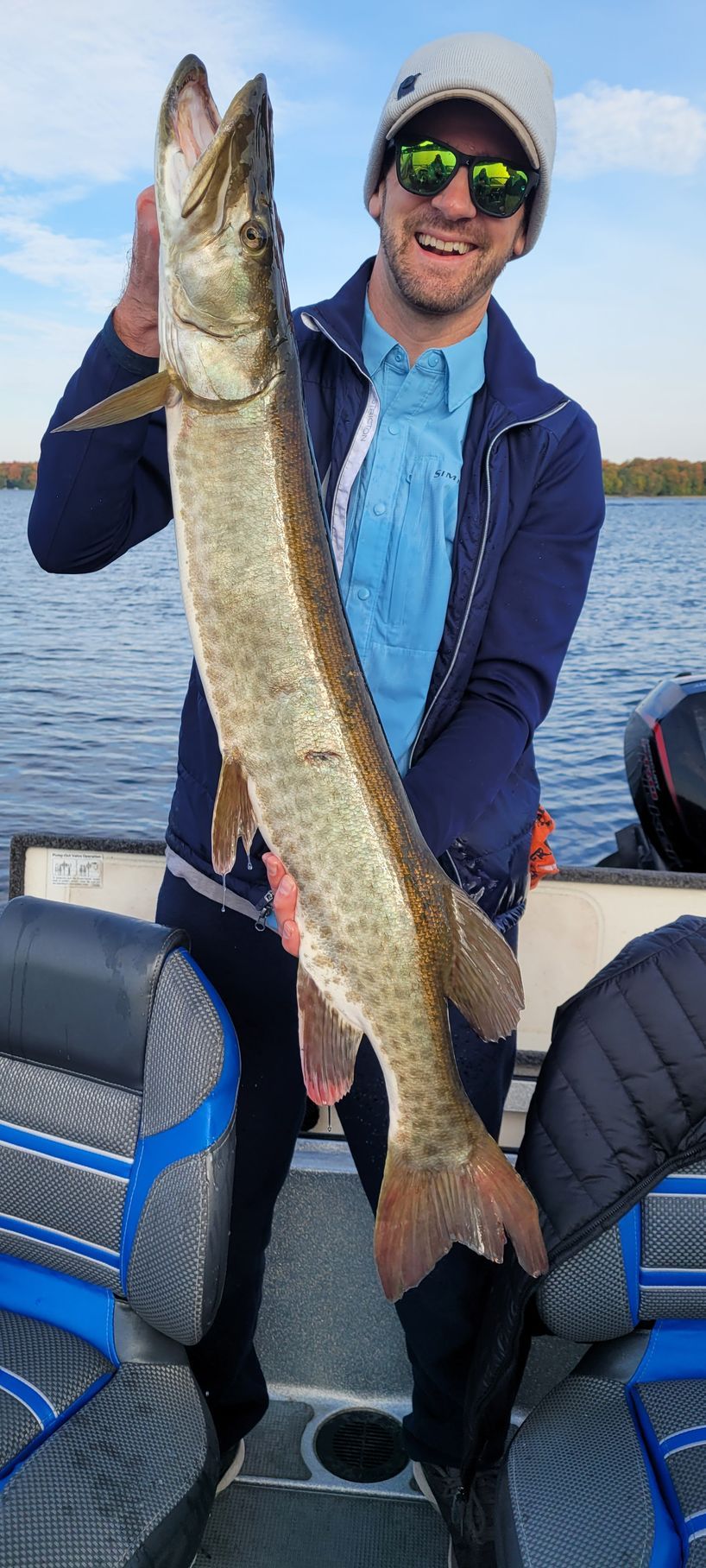 Angler on a boat holding a long fish upright on a calm blue lake