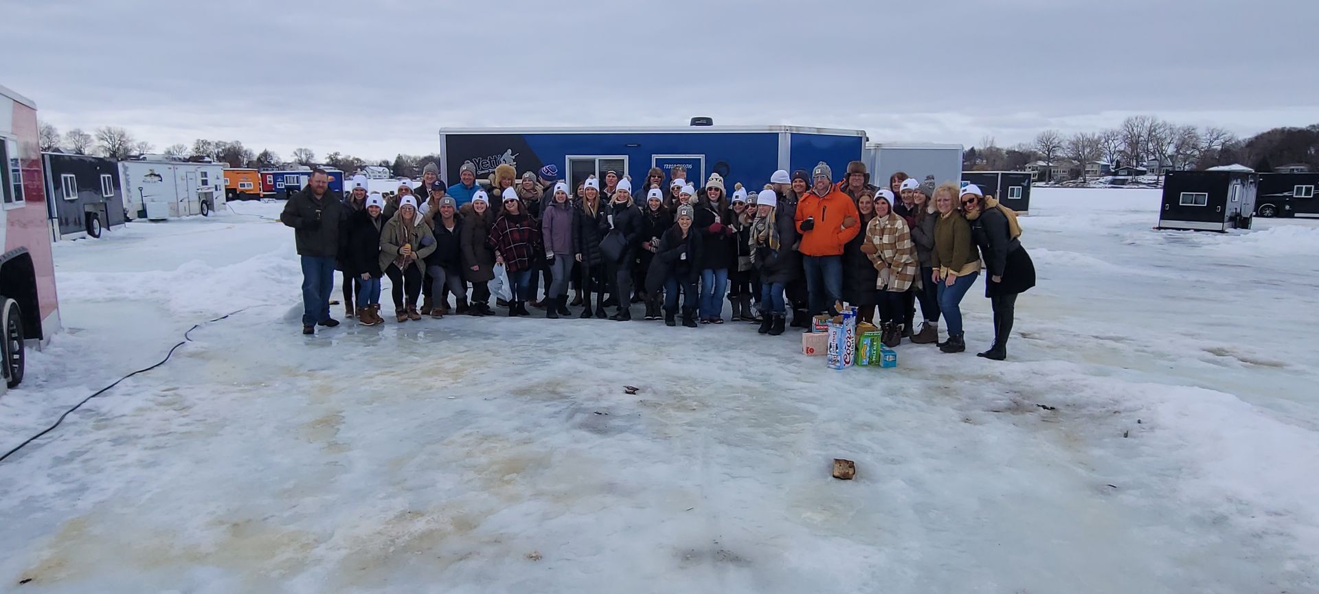 Large group posing outdoors on a snowy ice surface under a cloudy sky