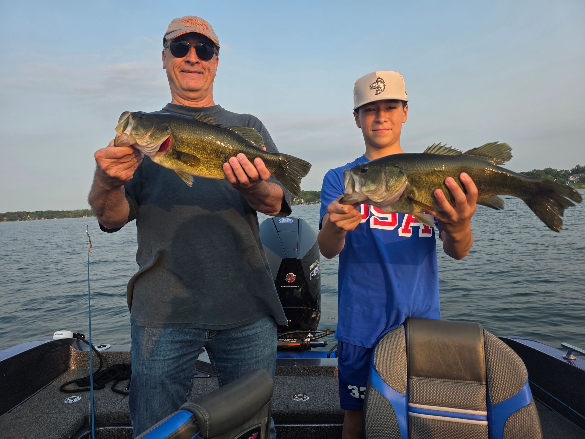 Two people on a boat holding large fish at sunset on a lake