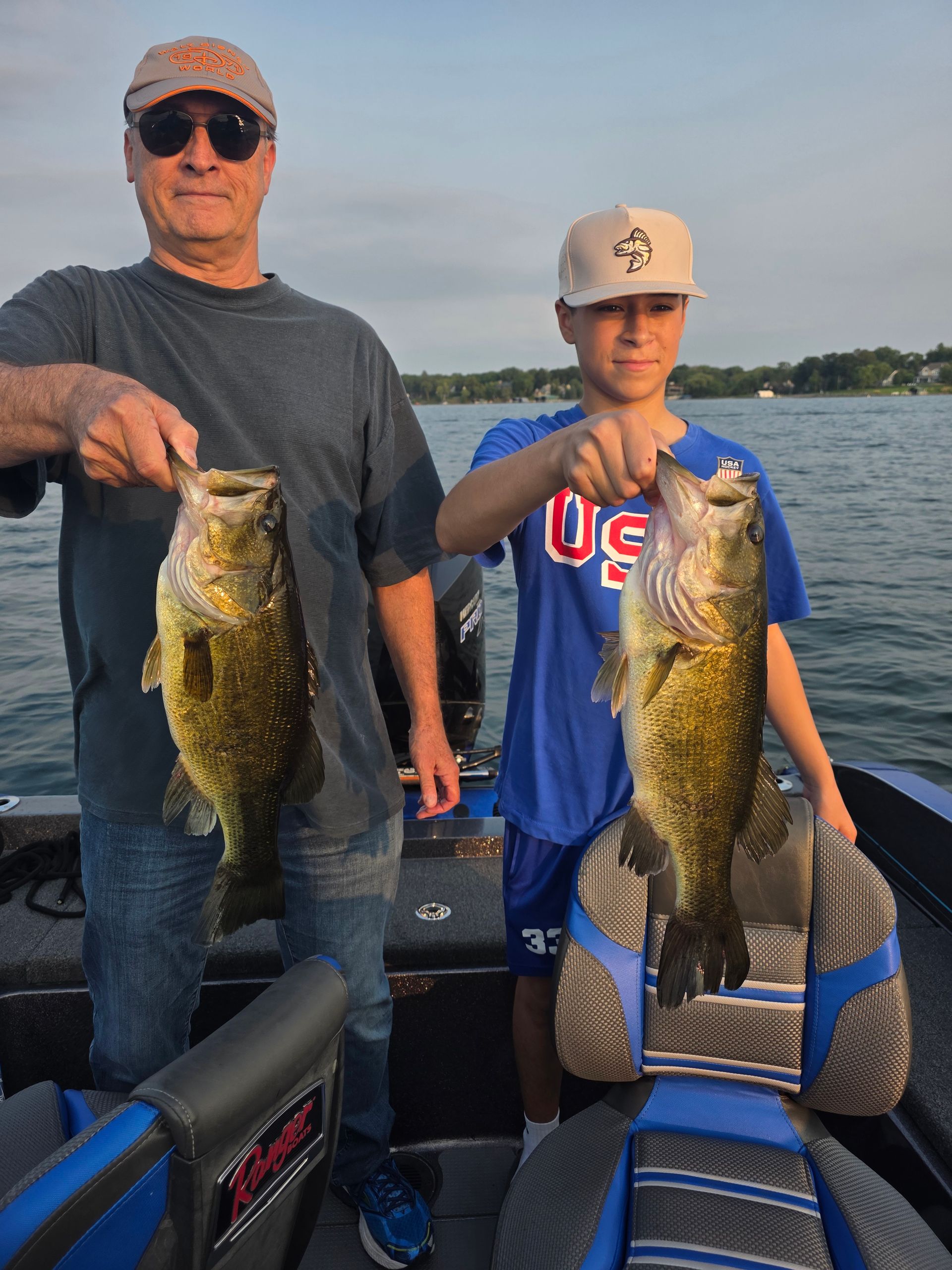 Two people on a boat holding up large fish at sunset on a lake