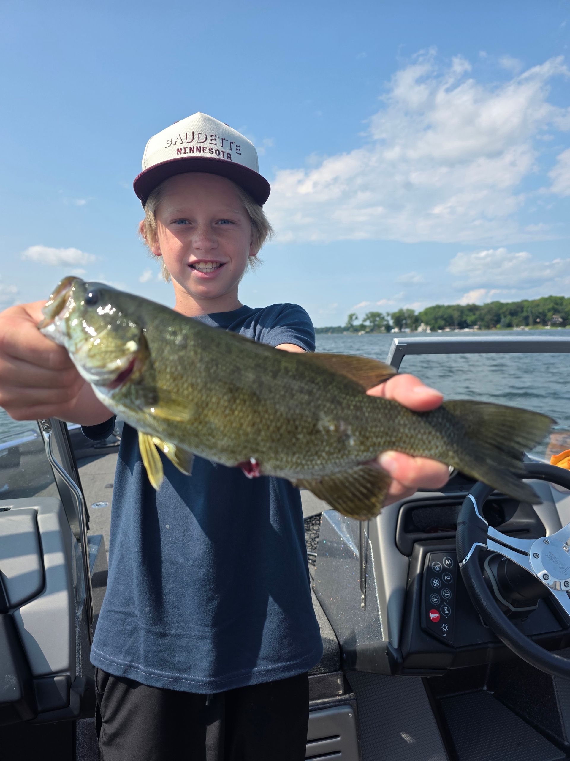 Person on a boat holding a large fish, smiling on a sunny day