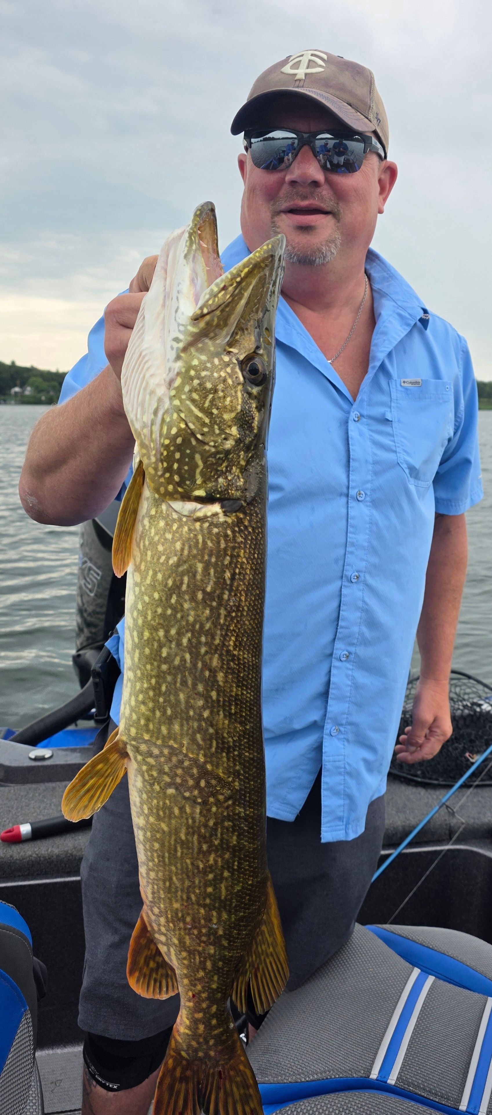 Man holding a large fish on a boat, wearing a blue shirt and cap