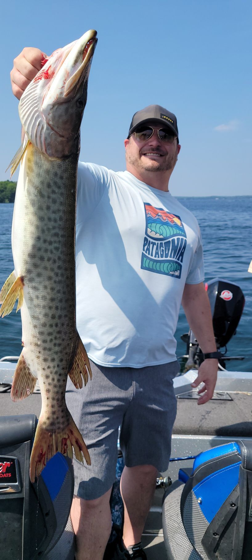 Man holding a large fish on a boat under a sunny blue sky