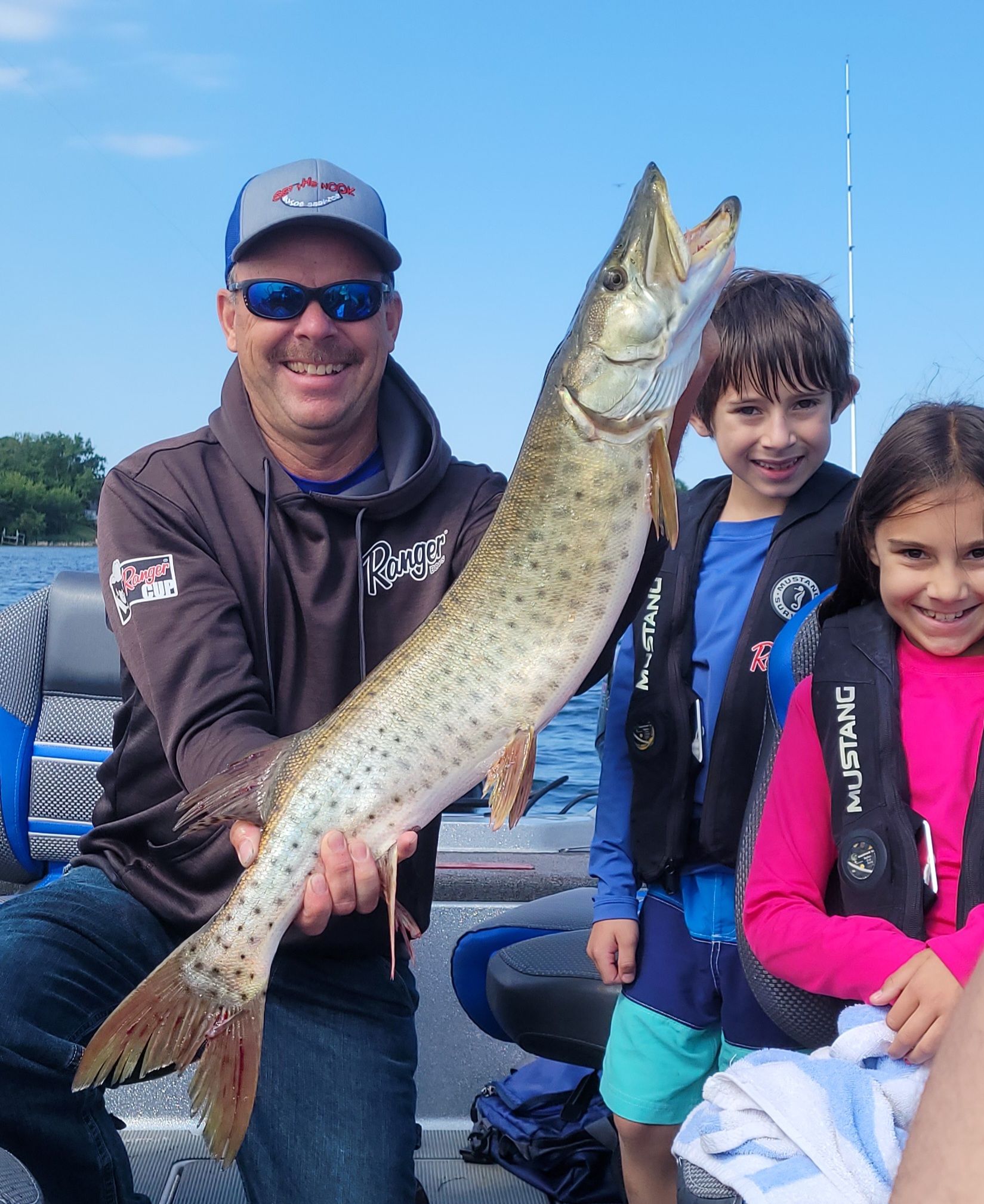 People on a boat holding a large fish, smiling on a sunny day on the water