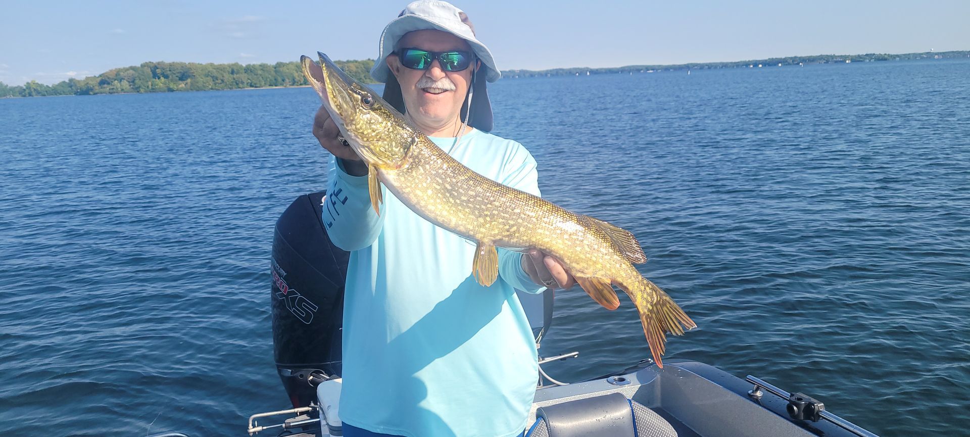 Person on a boat holding up a large fish on open water under a clear sky
