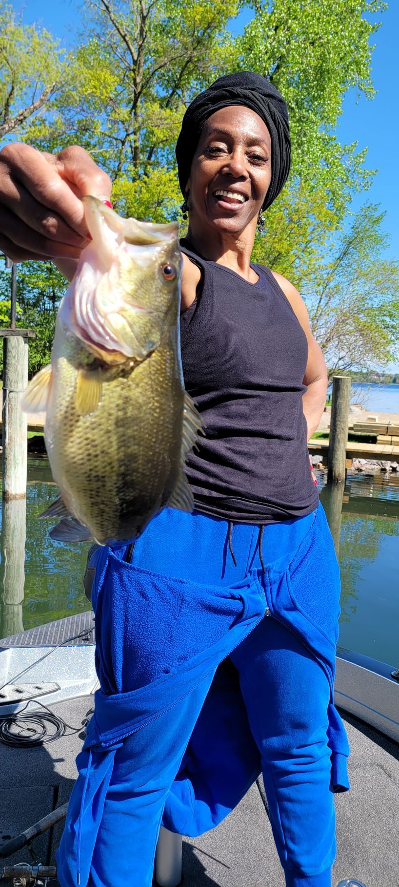 Person smiling and holding up a large fish on a dock by the water