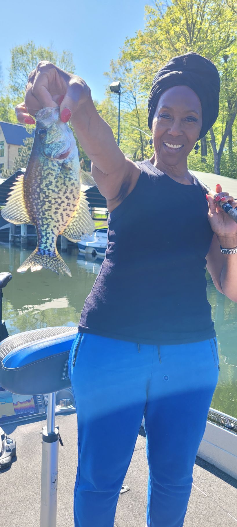 Smiling person holding up a large fish outdoors near a boat on a sunny day