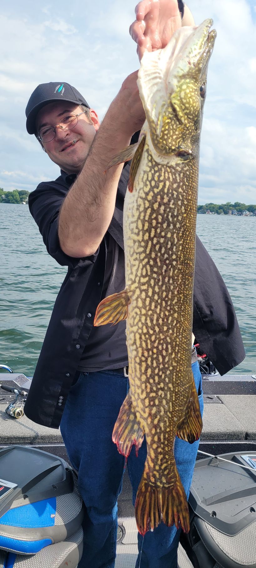 Person on a boat holding a large fish over the water, with another boat in the background.