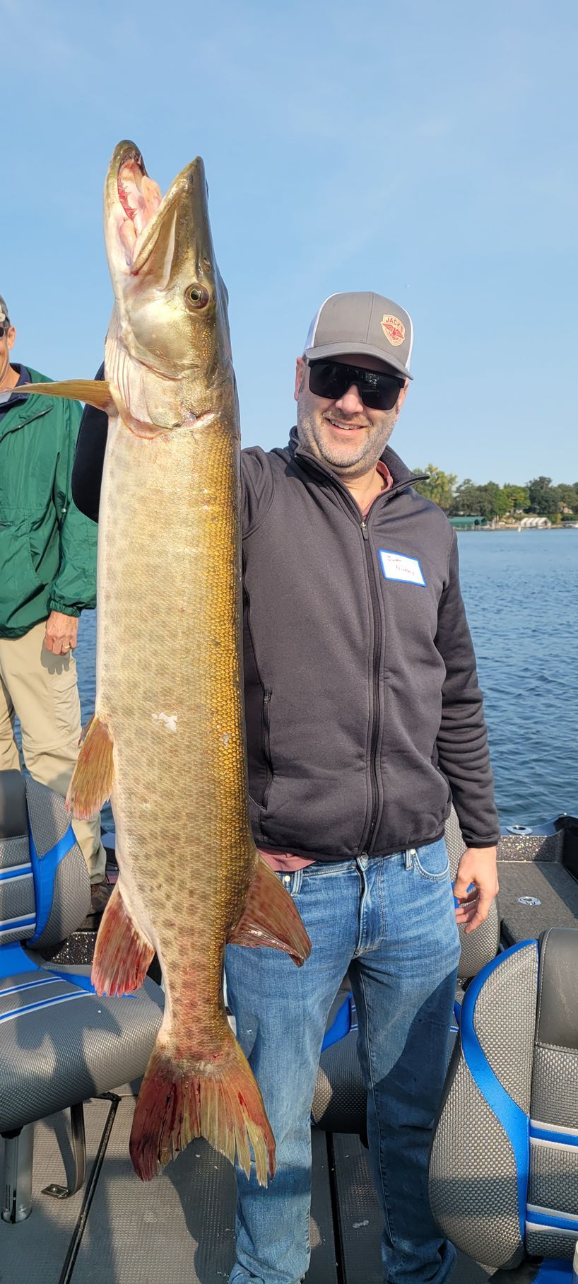 Smiling angler holding a large fish on a boat by the water on a sunny day