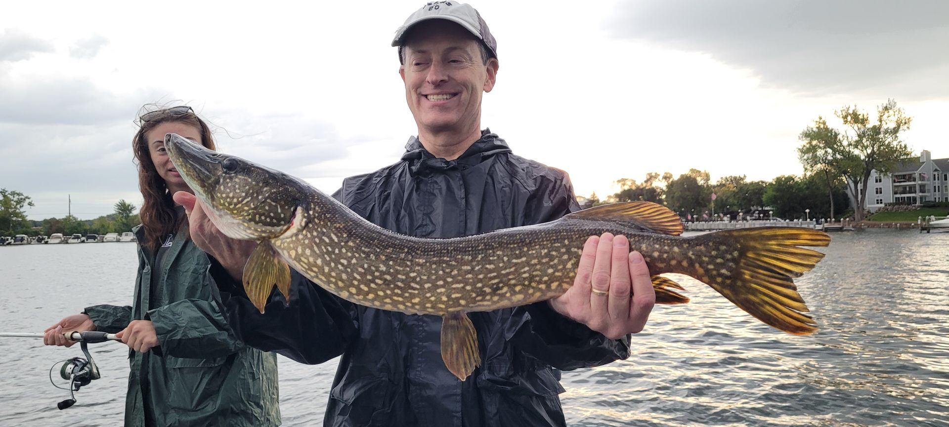 Person holding a large spotted fish while standing in a boat on a lake at sunset