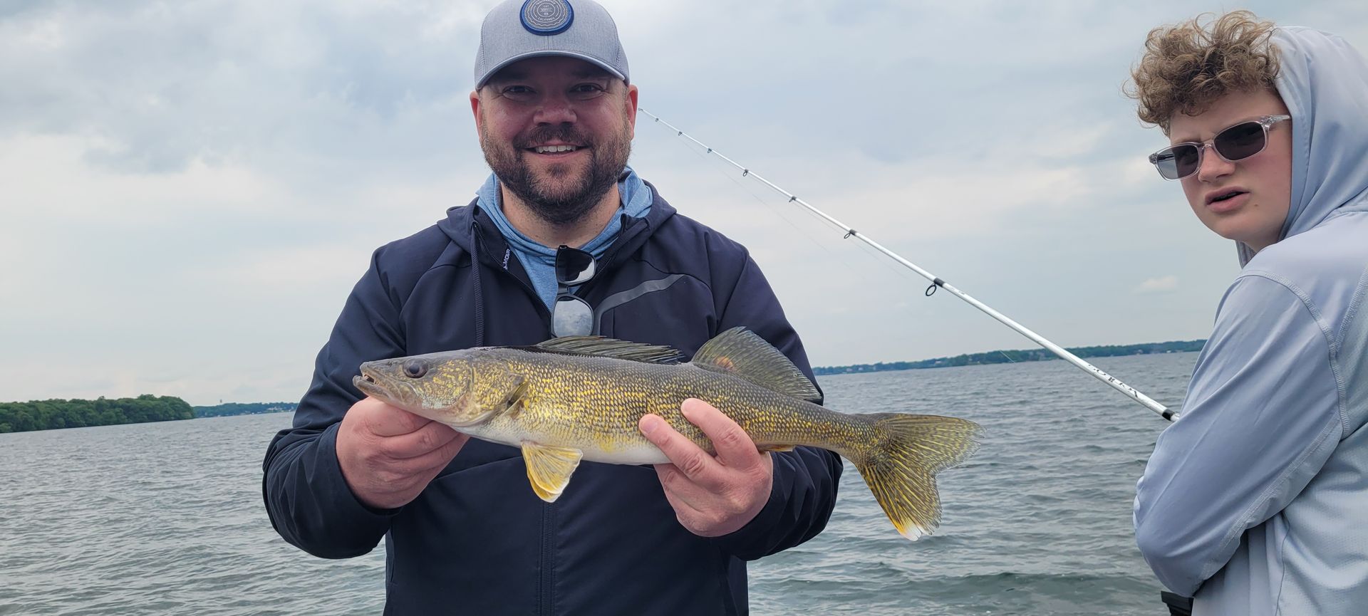Two anglers on a boat holding a speckled fish on a cloudy lake