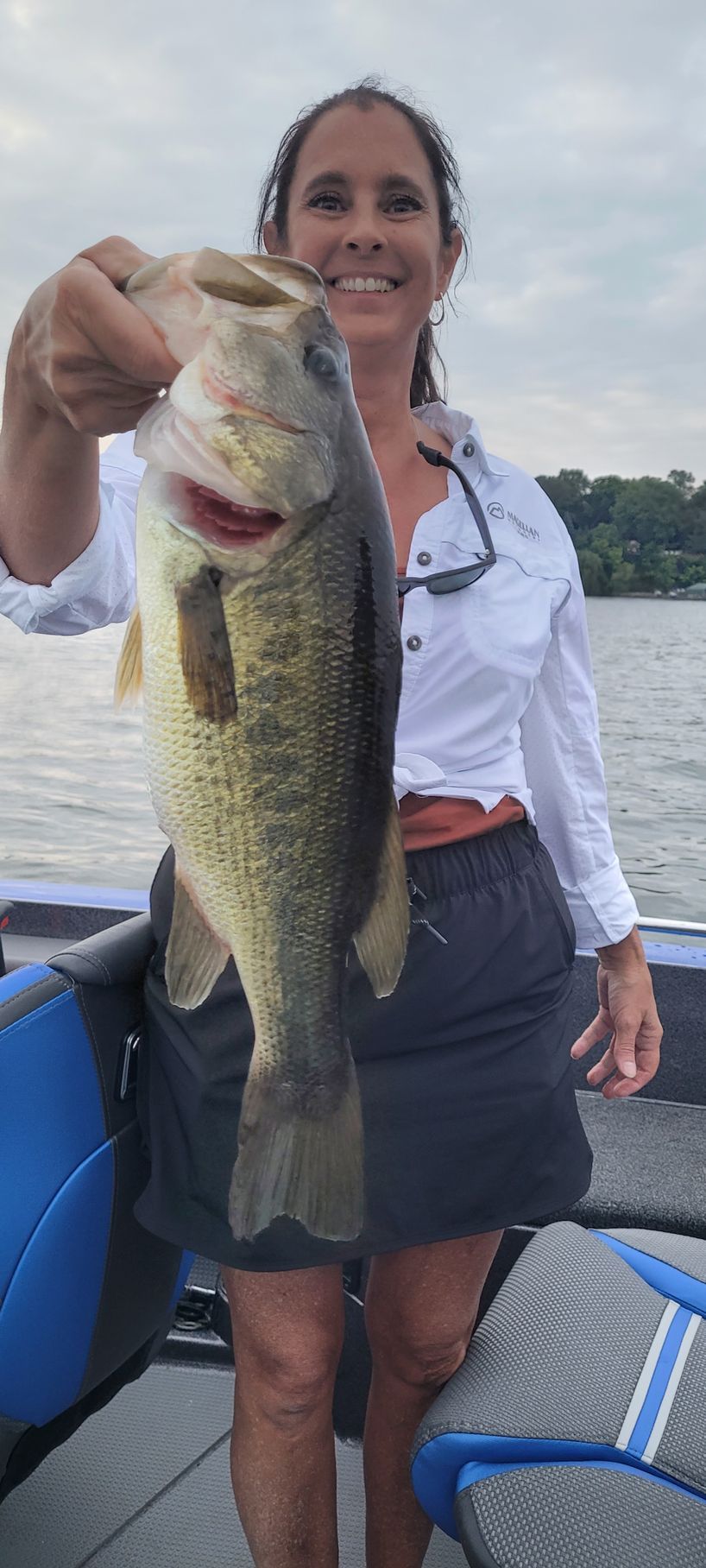 Woman holding up a large bass on a boat with water in the background
