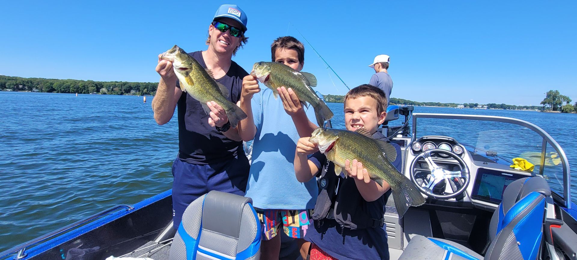 Three people on a boat holding up fish on a sunny lake
