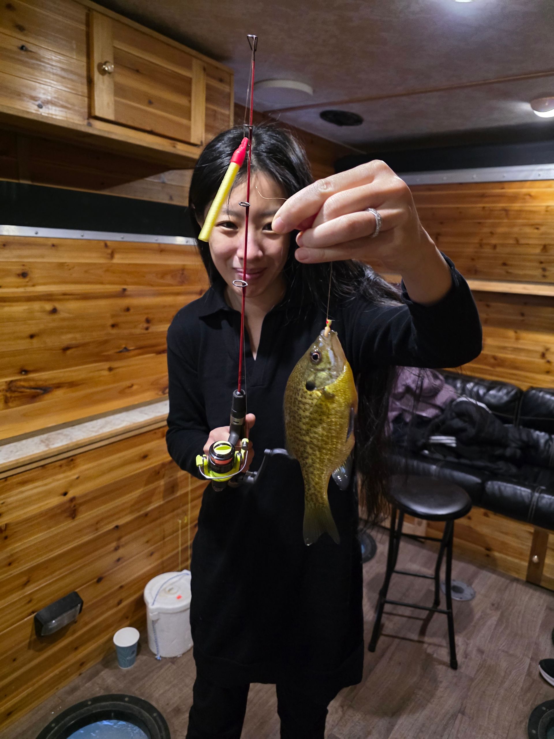 Person holding a fishing lure and a gold fish indoors in a wood-paneled room