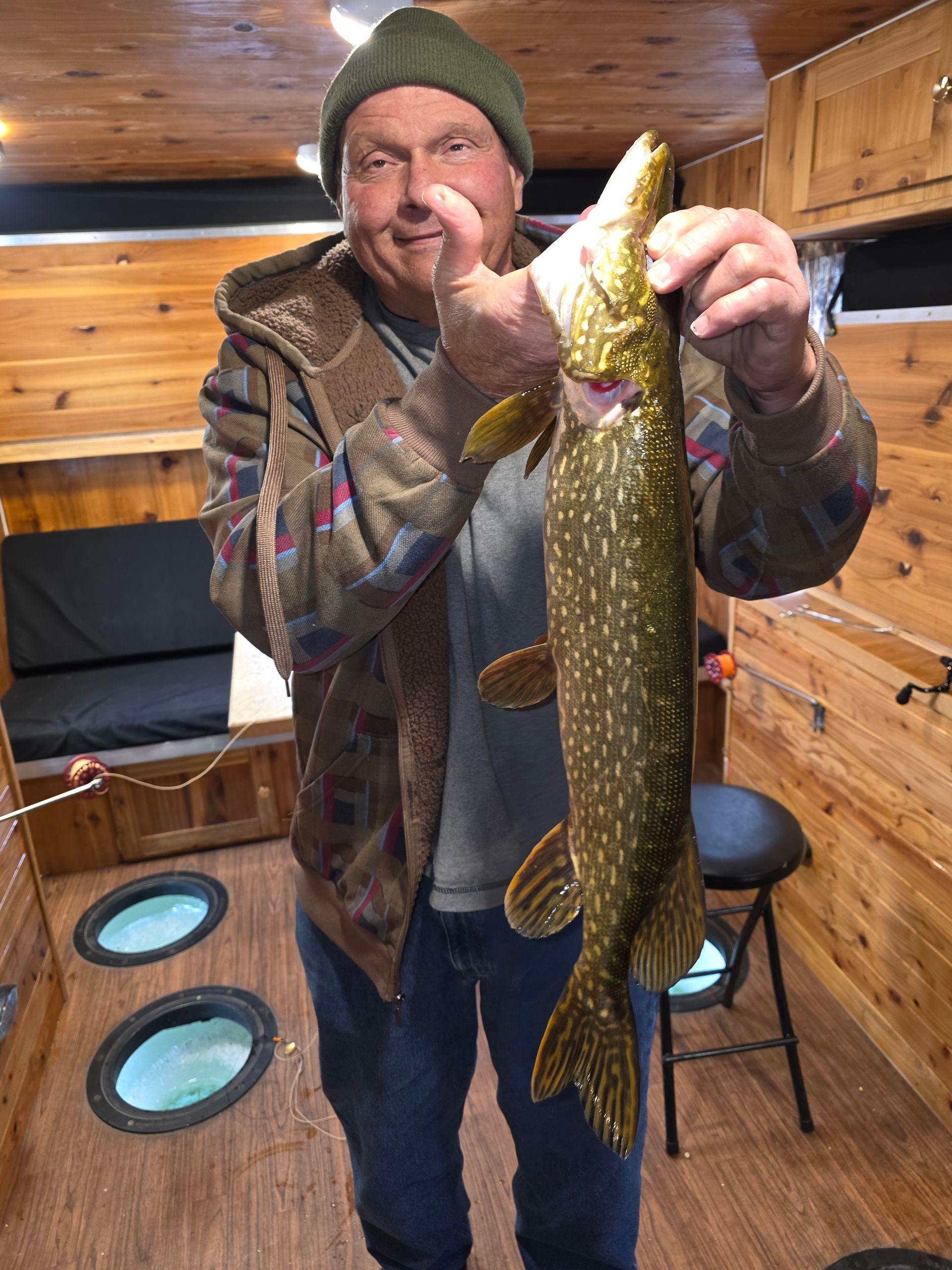 Man holding a large fish inside a wooden ice-fishing hut