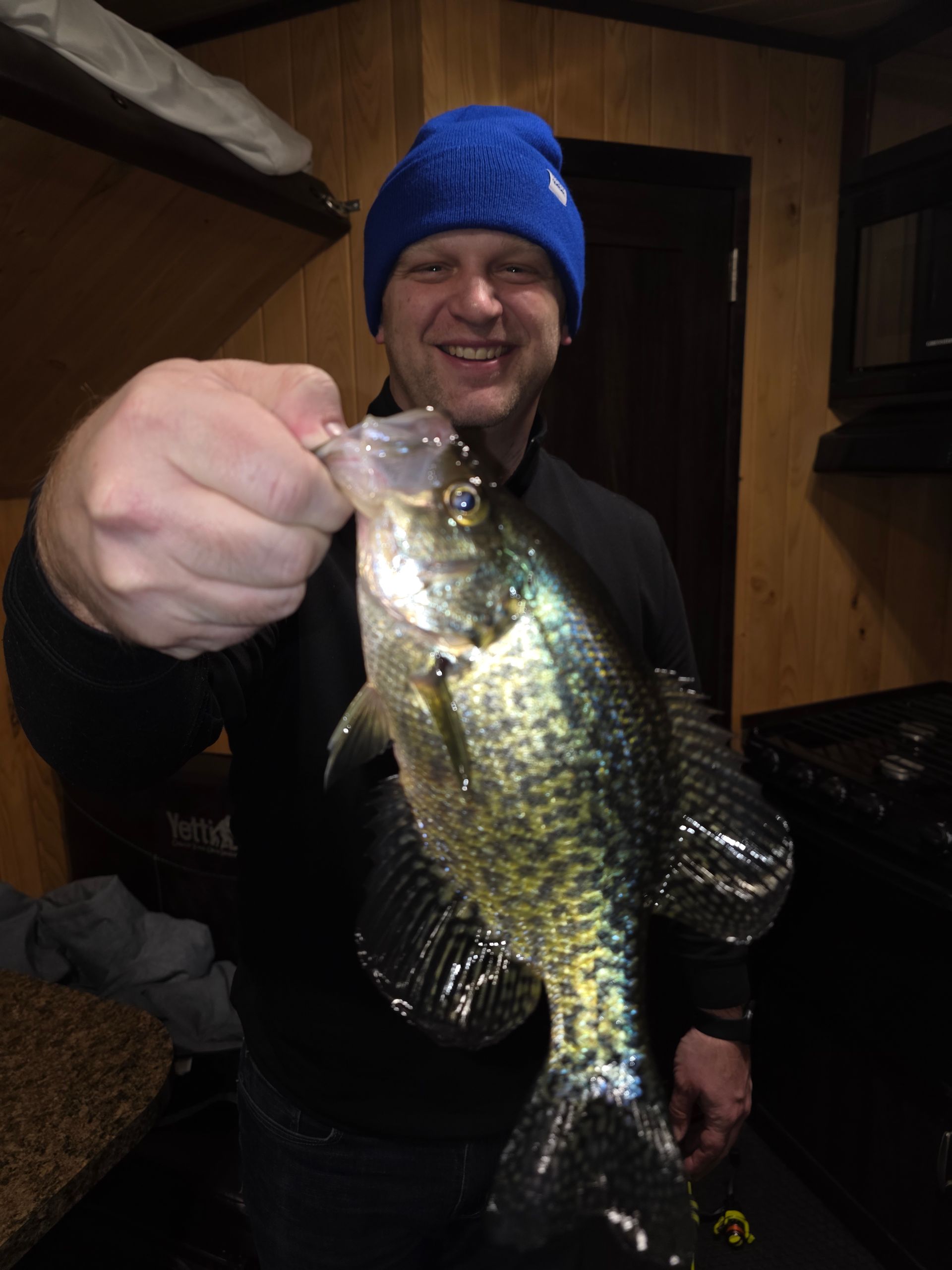 Person in blue beanie holding up a large crappie indoors.