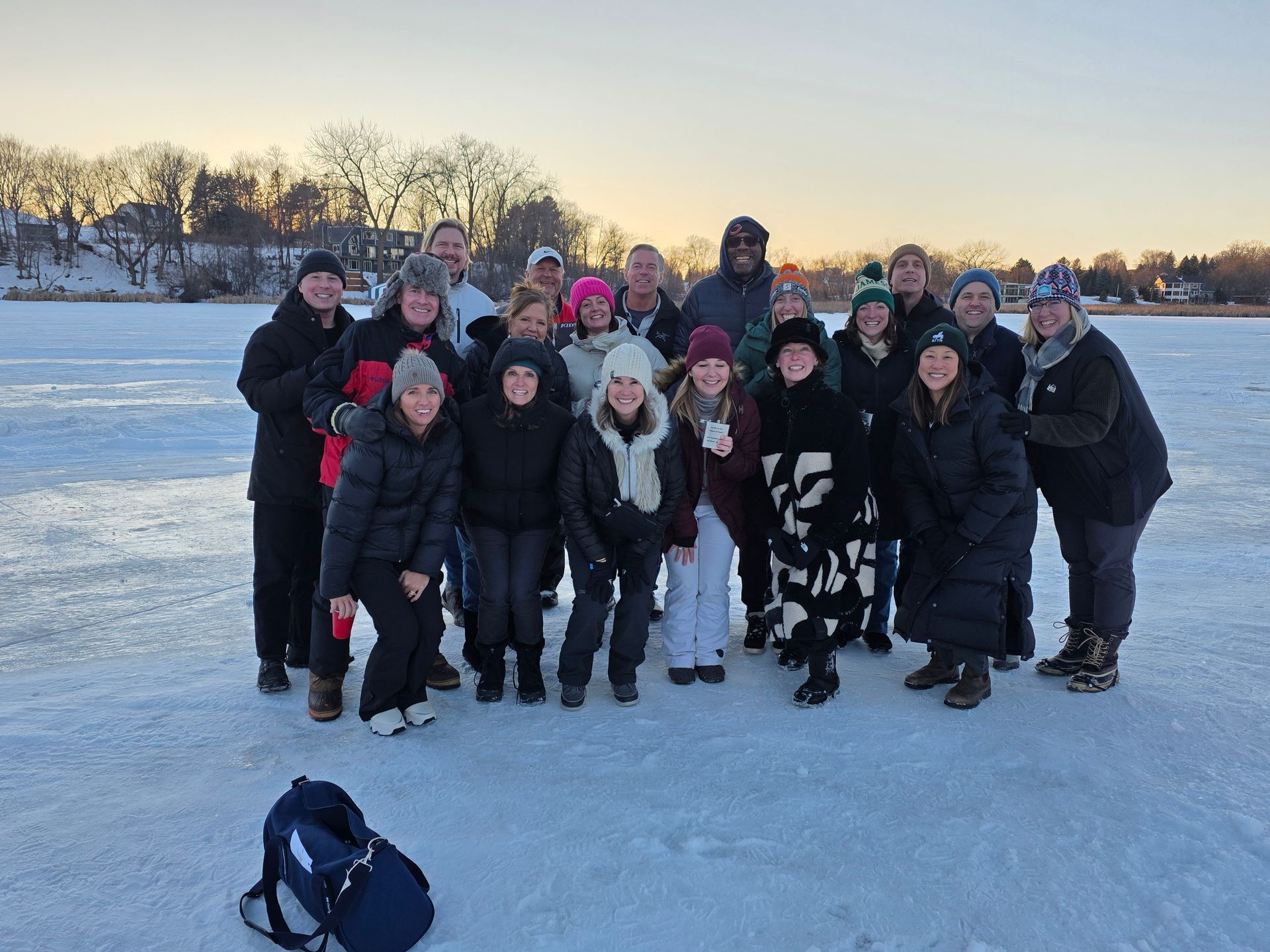 Group of bundled-up people posing on a snowy field at sunset, with trees in the background.